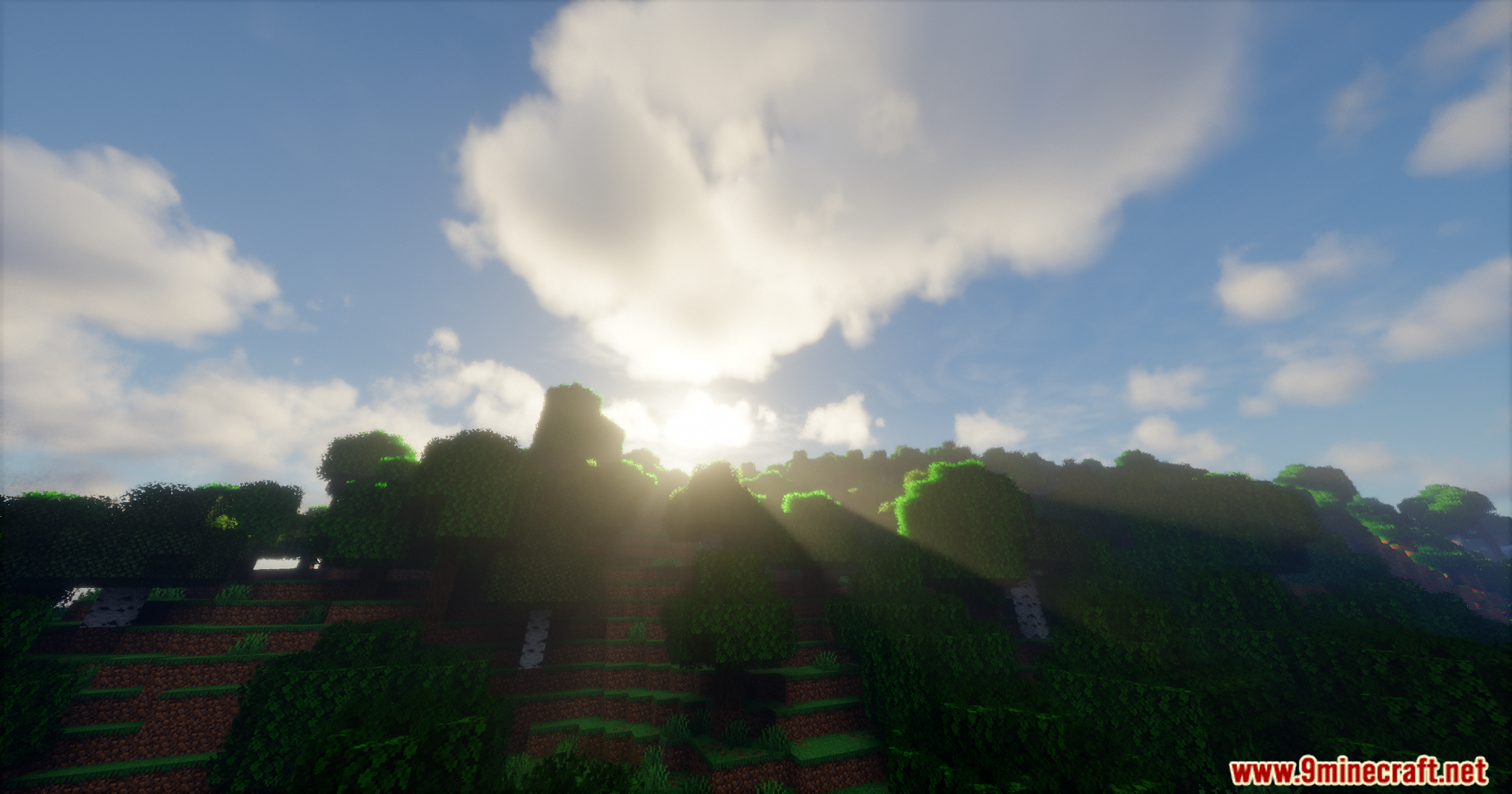 Bright sunbeams shining over a forested hill under a cloudy sky