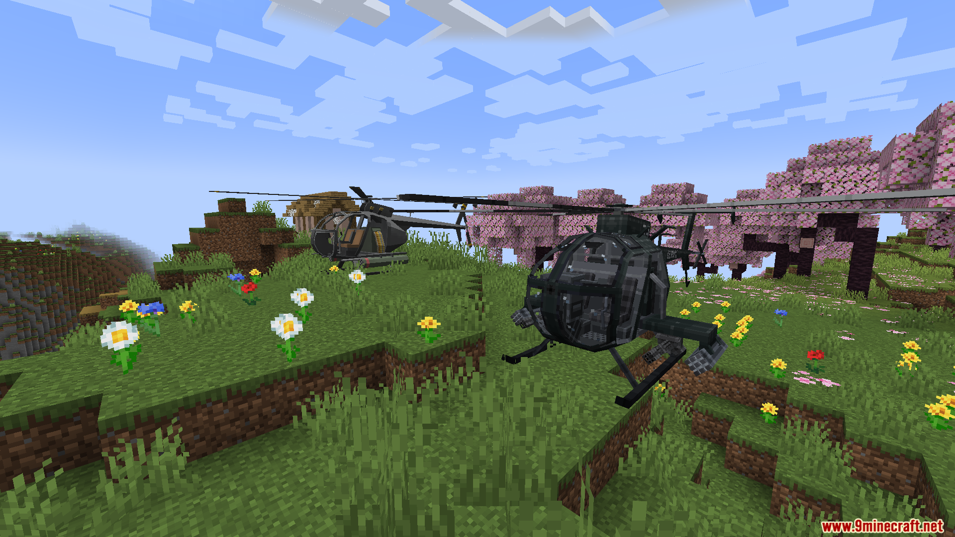 Two military helicopters parked in a grassy, flowery field