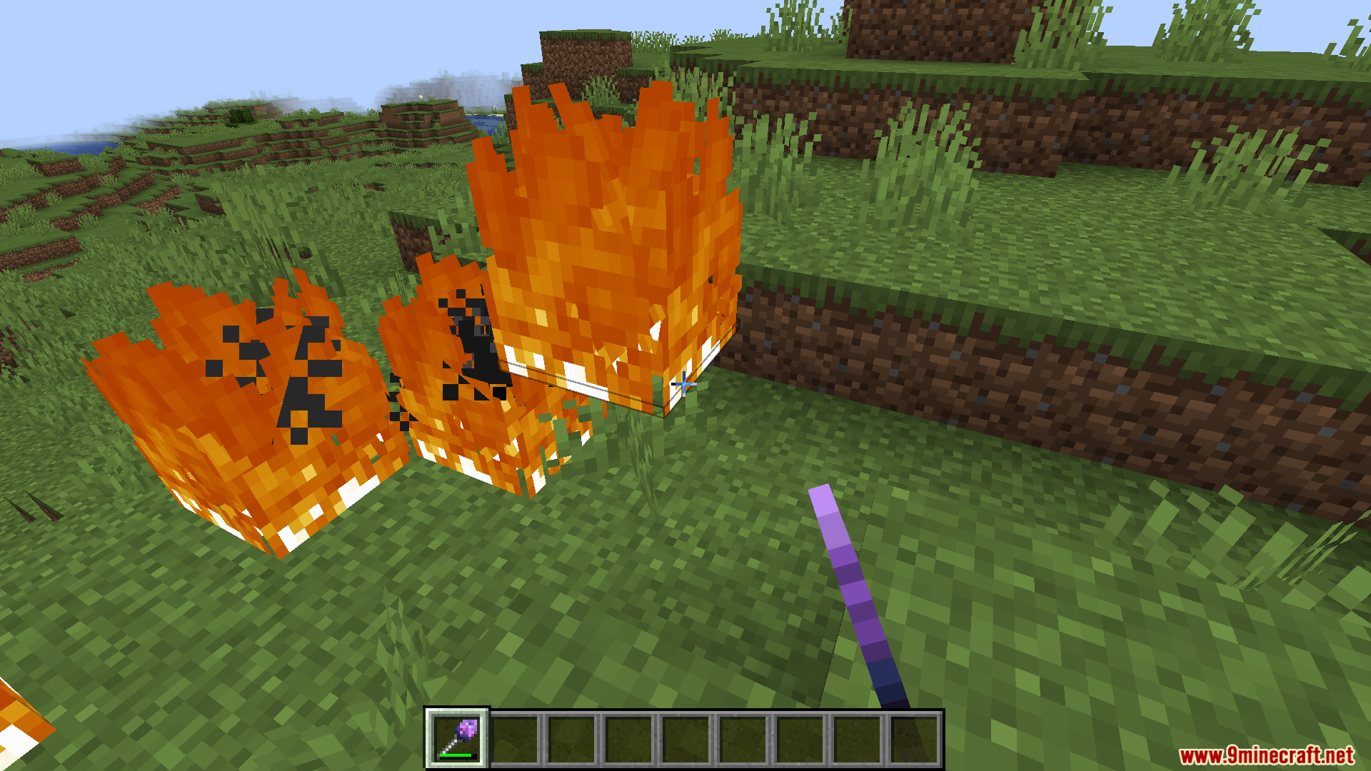 Player holding a purple magic wand near blocks of fire on the ground