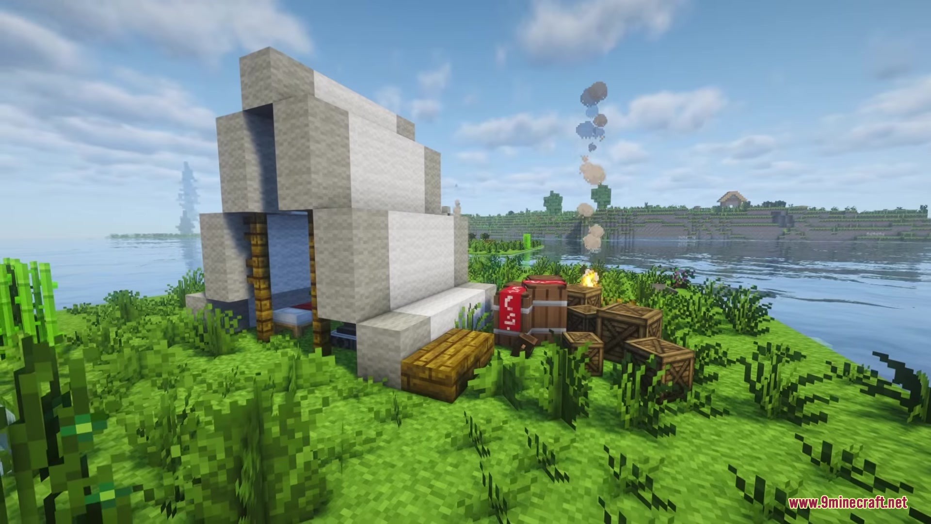 A white tent stands on a grassy shore with crates and campfire