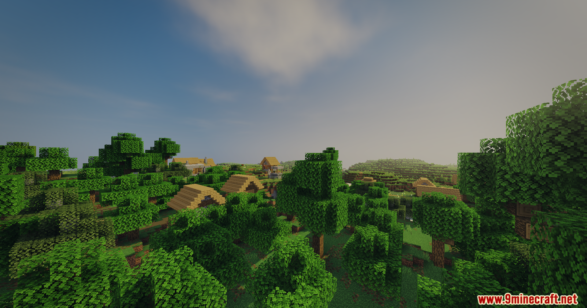 A small village nestled among dense green trees under a bright sunny sky