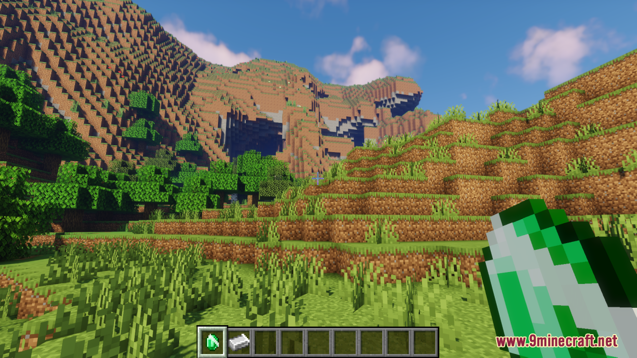 Player holding an animated emerald item in a scenic mountain landscape