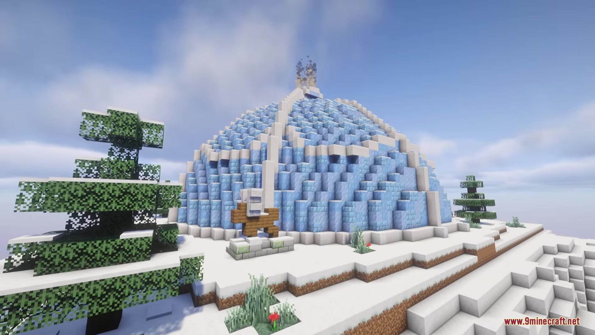 A massive ice dome structure sits on a snowy hill with spruce trees