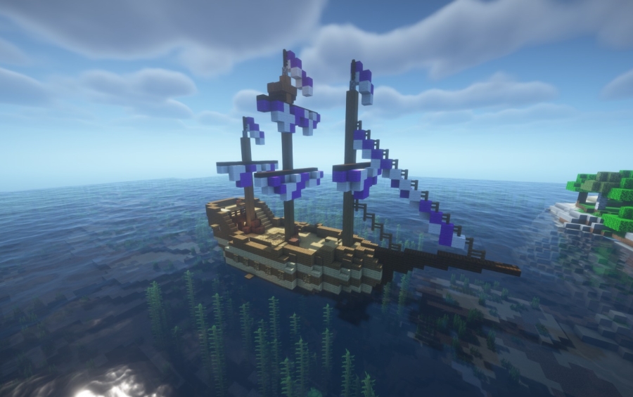 A medieval wooden ship with blue and white sails floating on the clear water