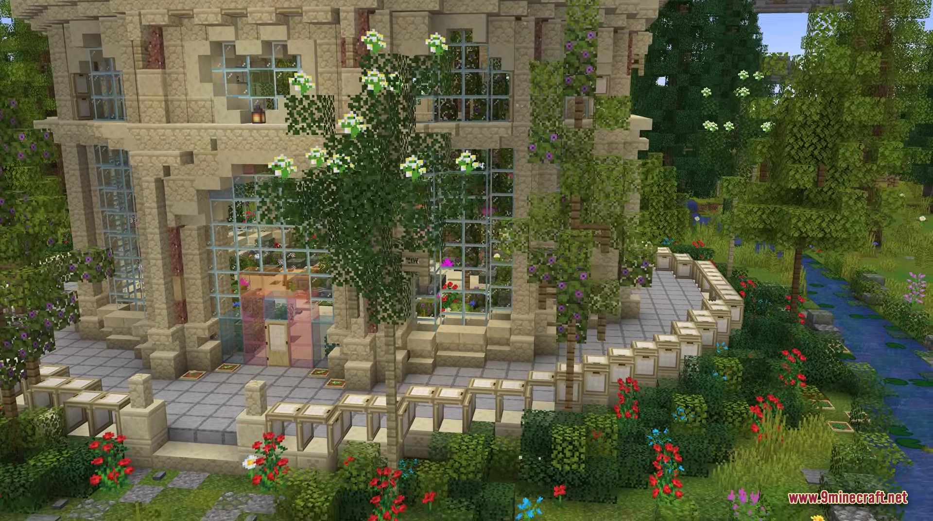 A detailed stone building with glass windows surrounded by lush gardens and flowers