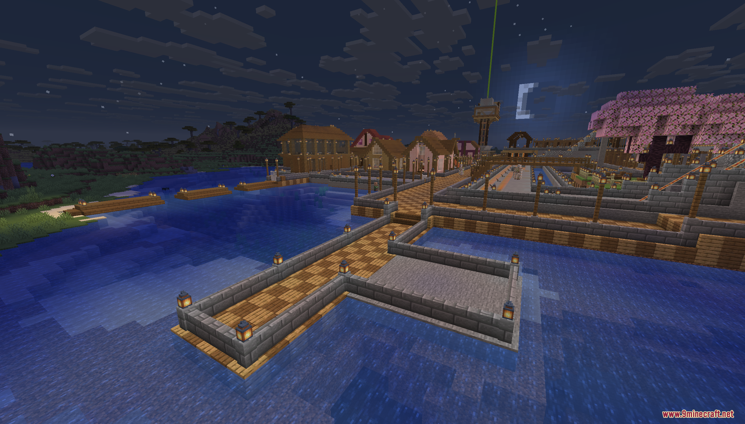 A stone dock extends into the ocean near a town at night