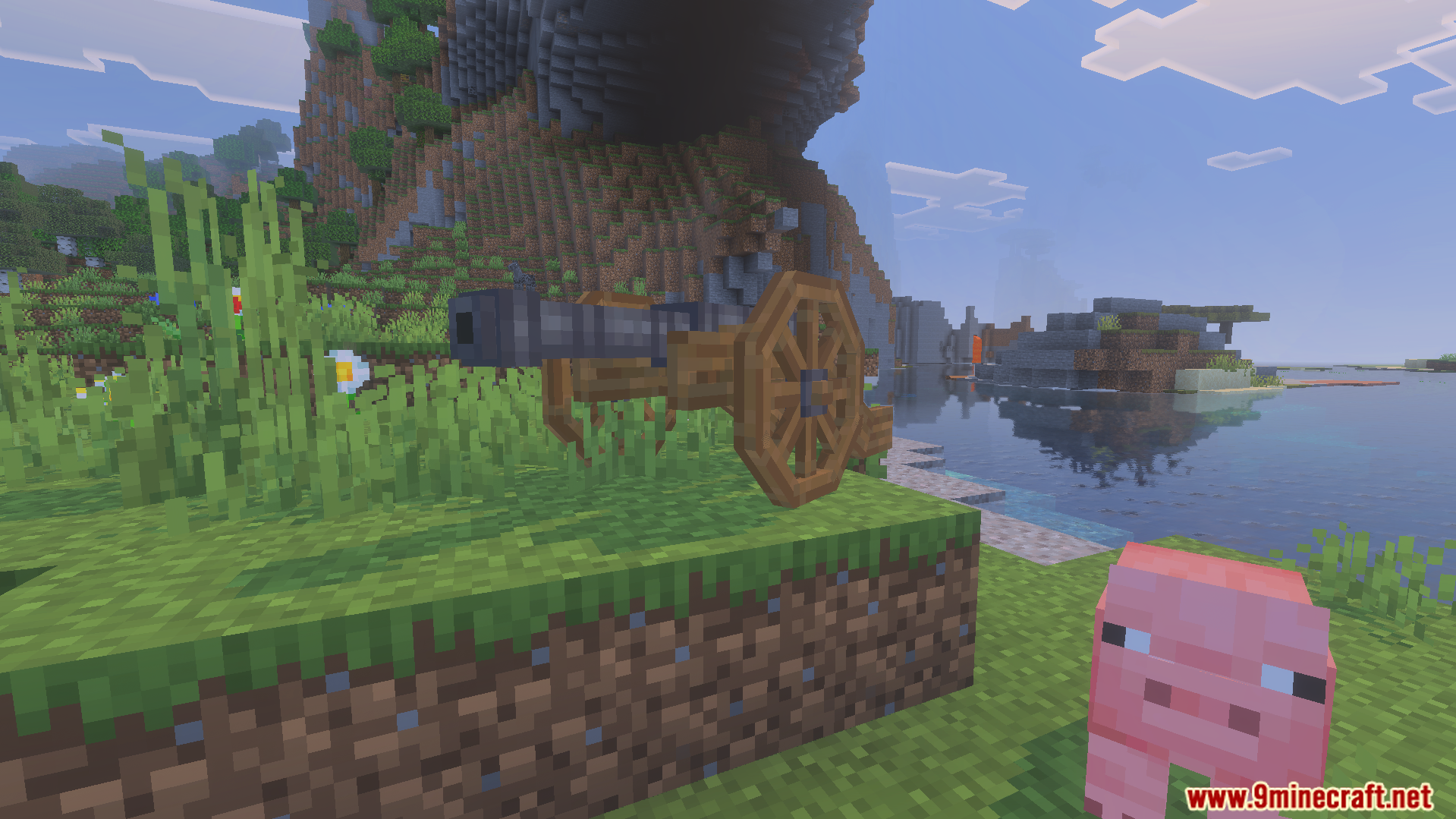 A wooden cannon sits on a grassy hill near a pink pig
