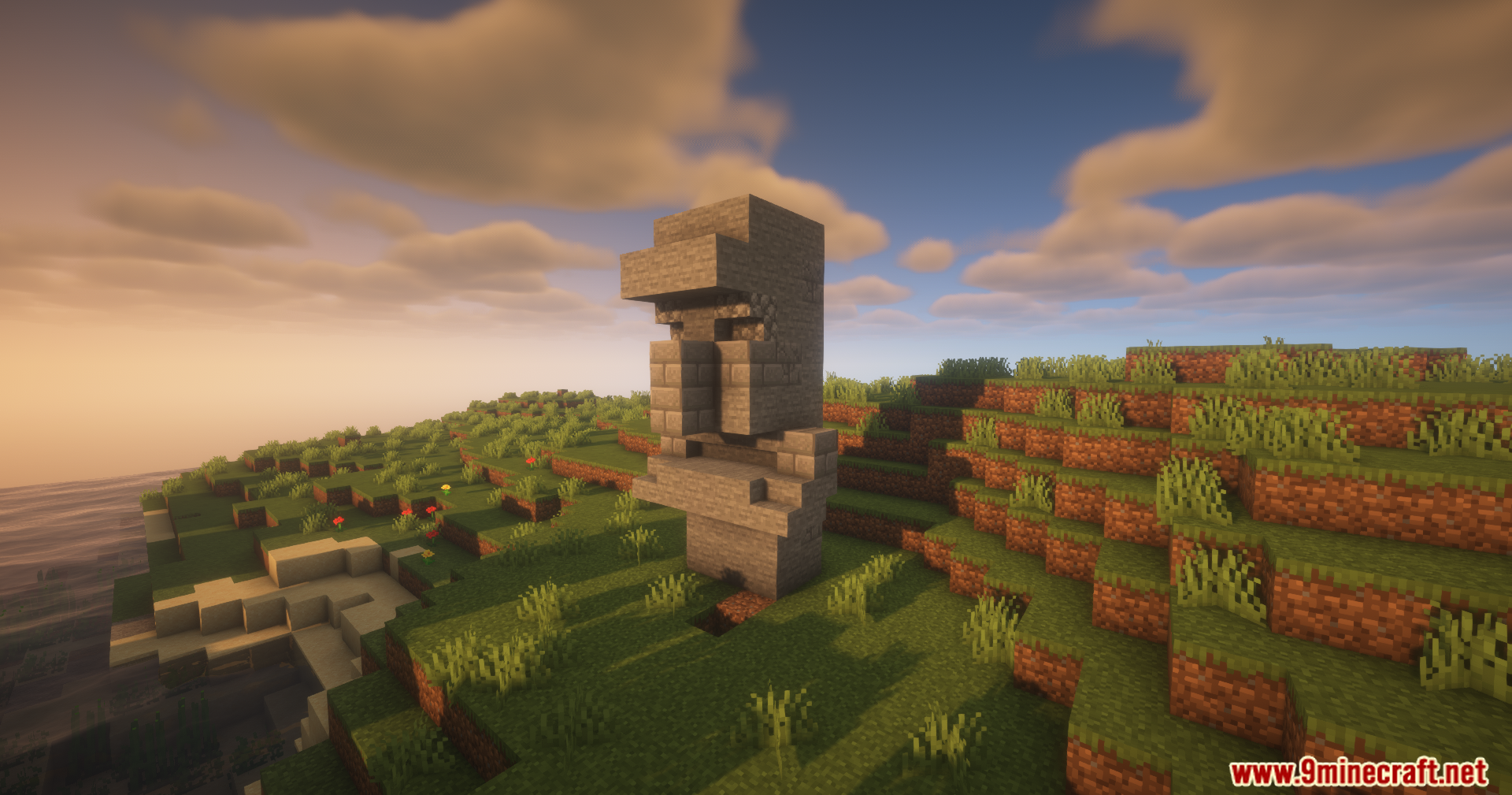 A large stone villager statue standing on a grassy hill at sunset