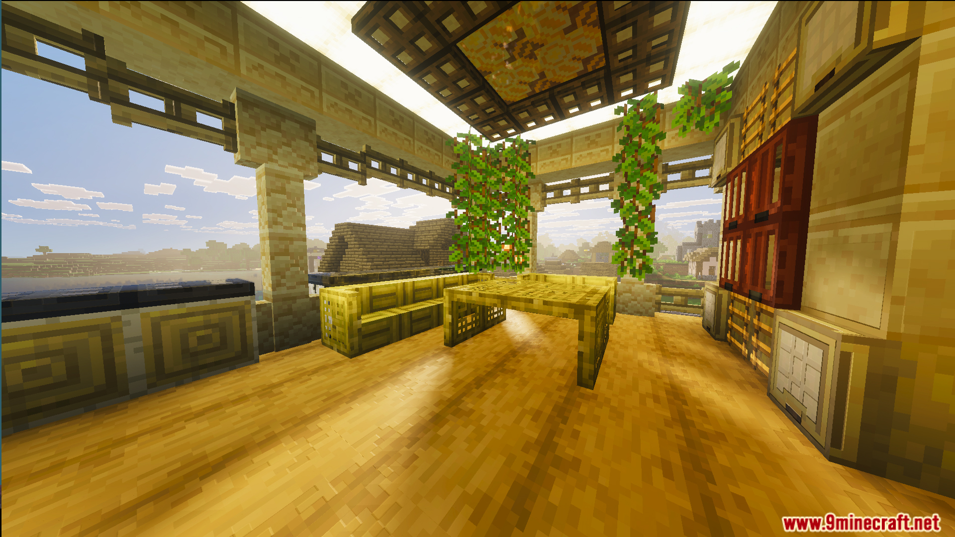 Sunlit balcony area with bamboo furniture and hanging vines overlooking a nearby village