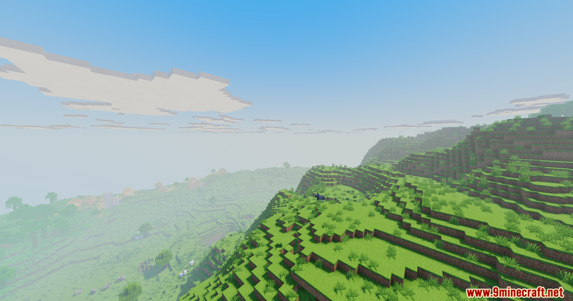 A scenic view of a grassy hillside with an animal and distant village