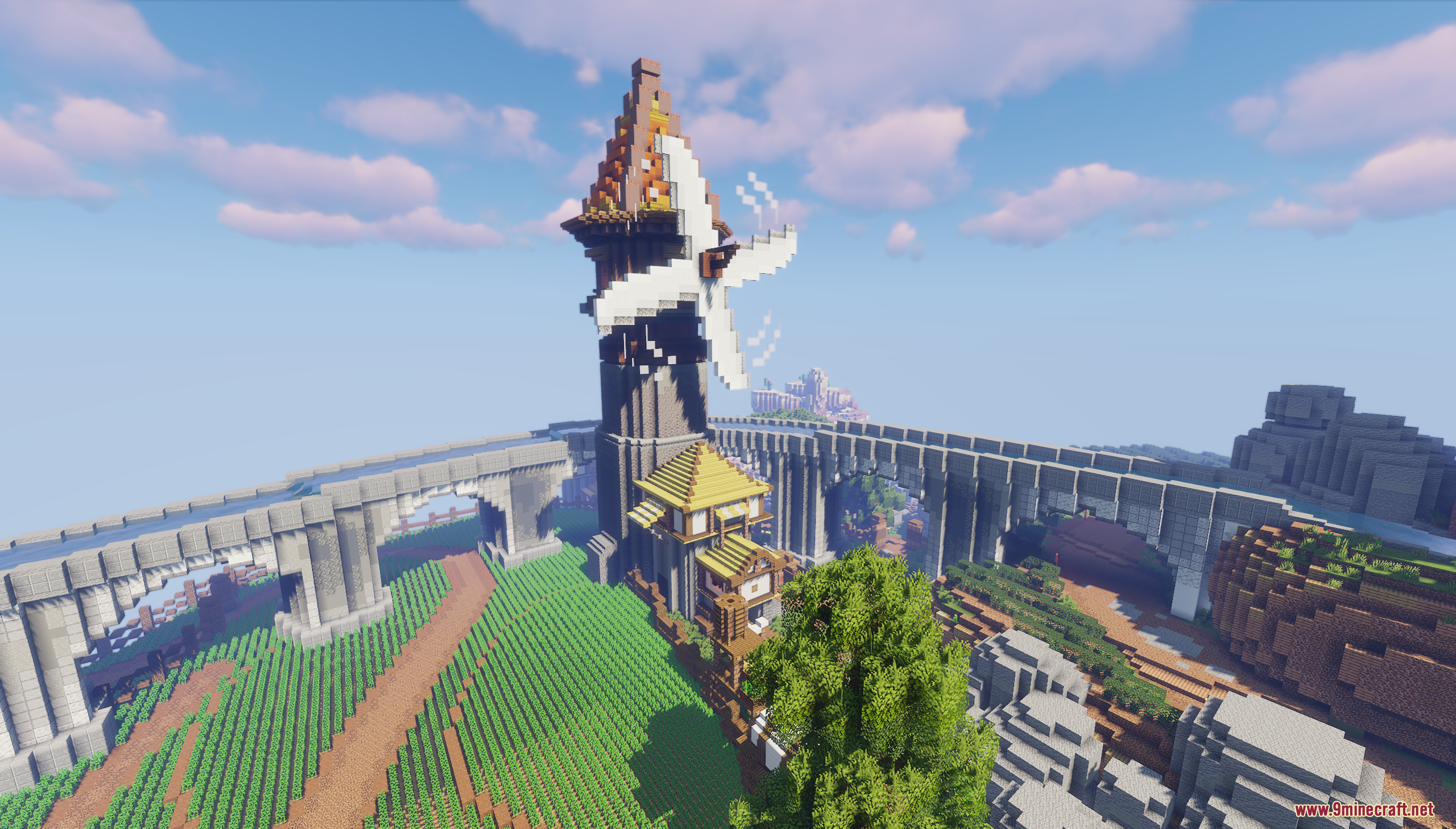 A tall windmill tower overlooks lush green fields and a large stone bridge
