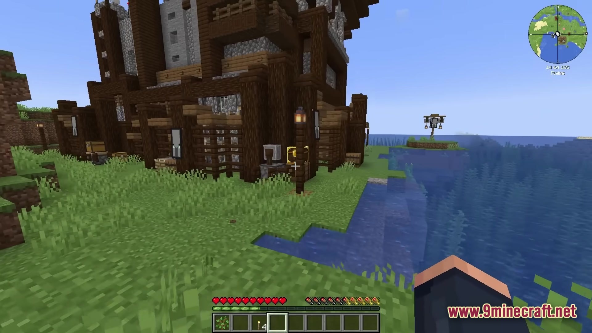 All The Mods 10 ATM10 Modpack Screenshot 1 A large wooden and stone outpost structure stands on a grassy shoreline next to the ocean