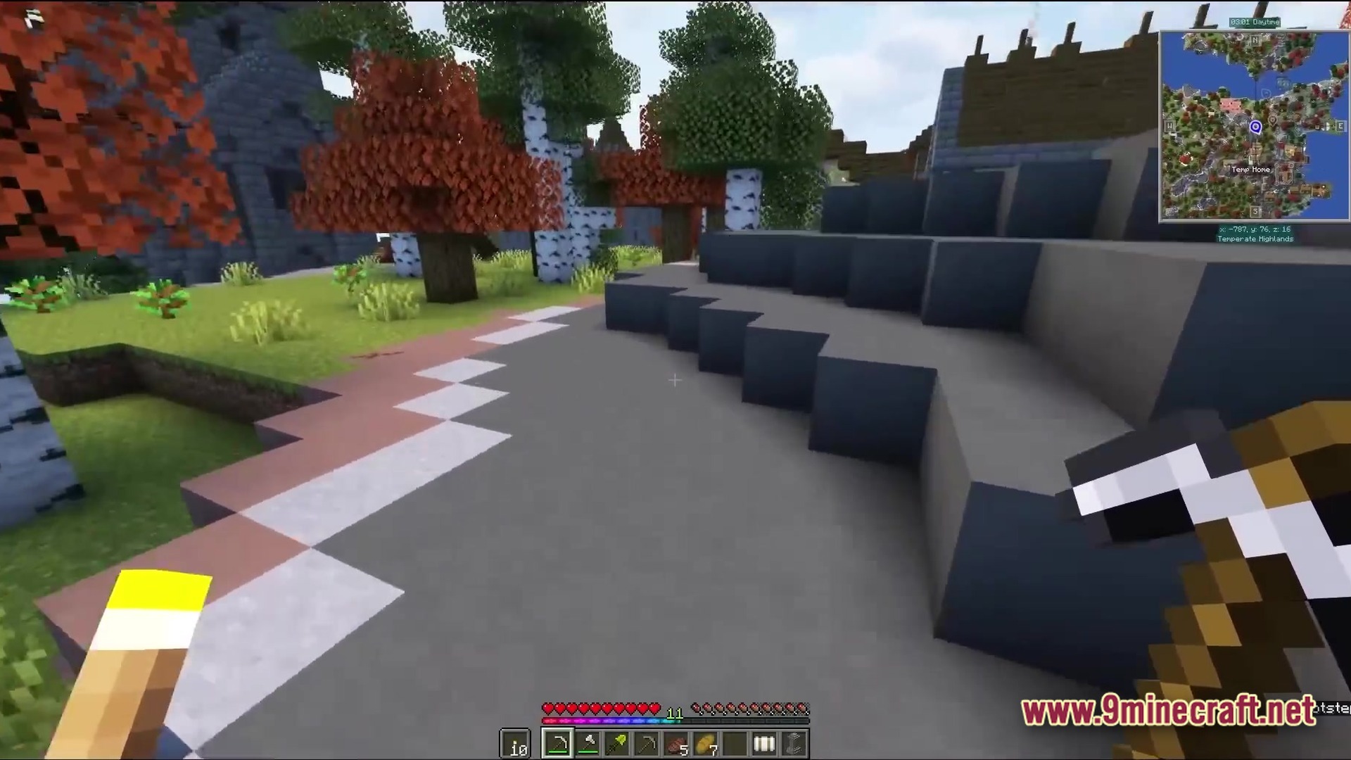 A player holds a pickaxe near stone cliffs and autumn trees in a temperate highlands biome
