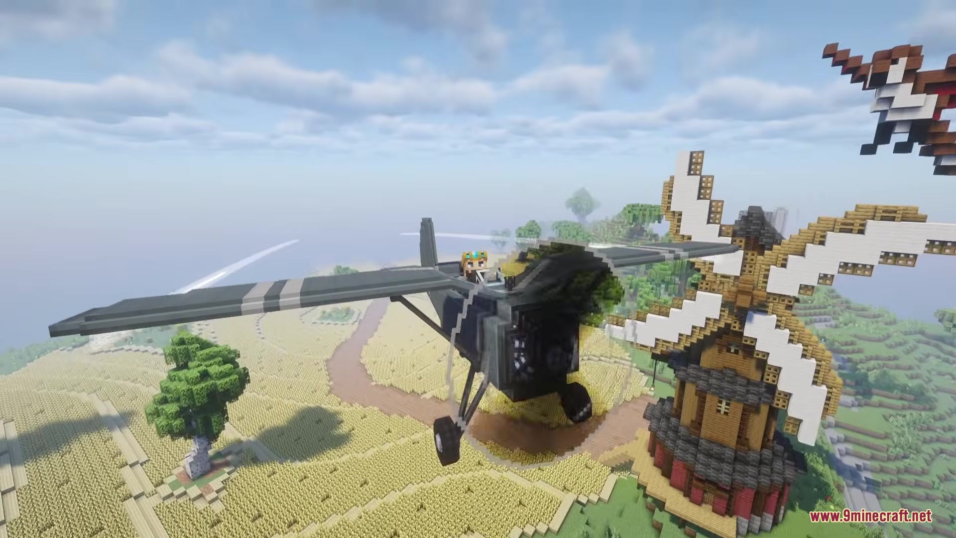 A player pilots a grey airplane past a windmill over a wheat field