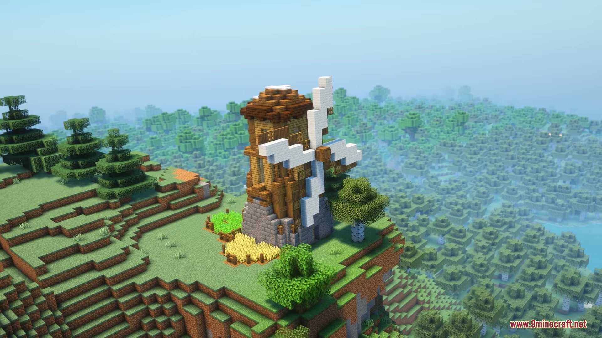 A scenic view of a wooden windmill built on a grassy cliff