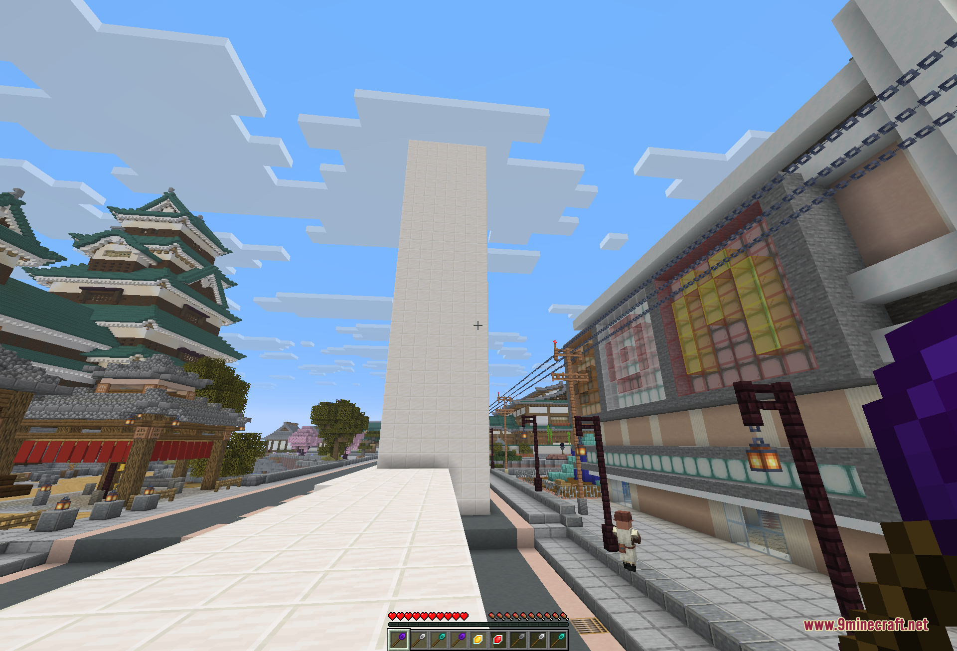 A tall white pillar built straight up along a paved street, standing between a castle keep and a row of townhouses
