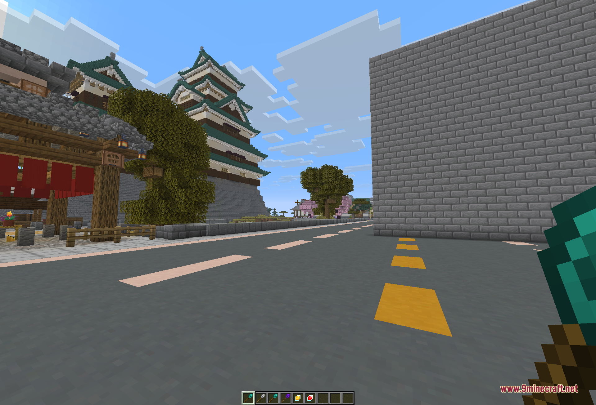A long grey stone-brick wall extended along a road in a single click, with a castle keep, trees, and cherry blossoms in the distance