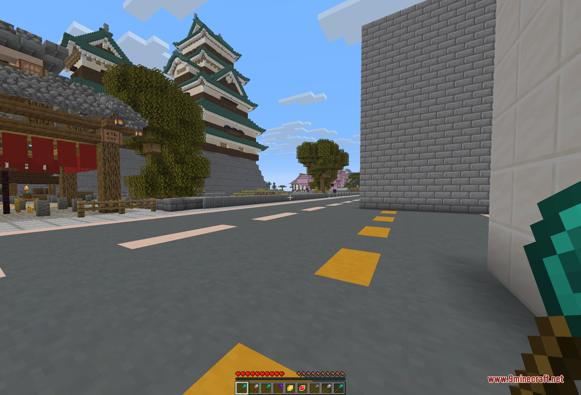 A themed city street lined with a tall grey wall on the right and a green-roofed castle on the left, showing a wall run built quickly with the wand