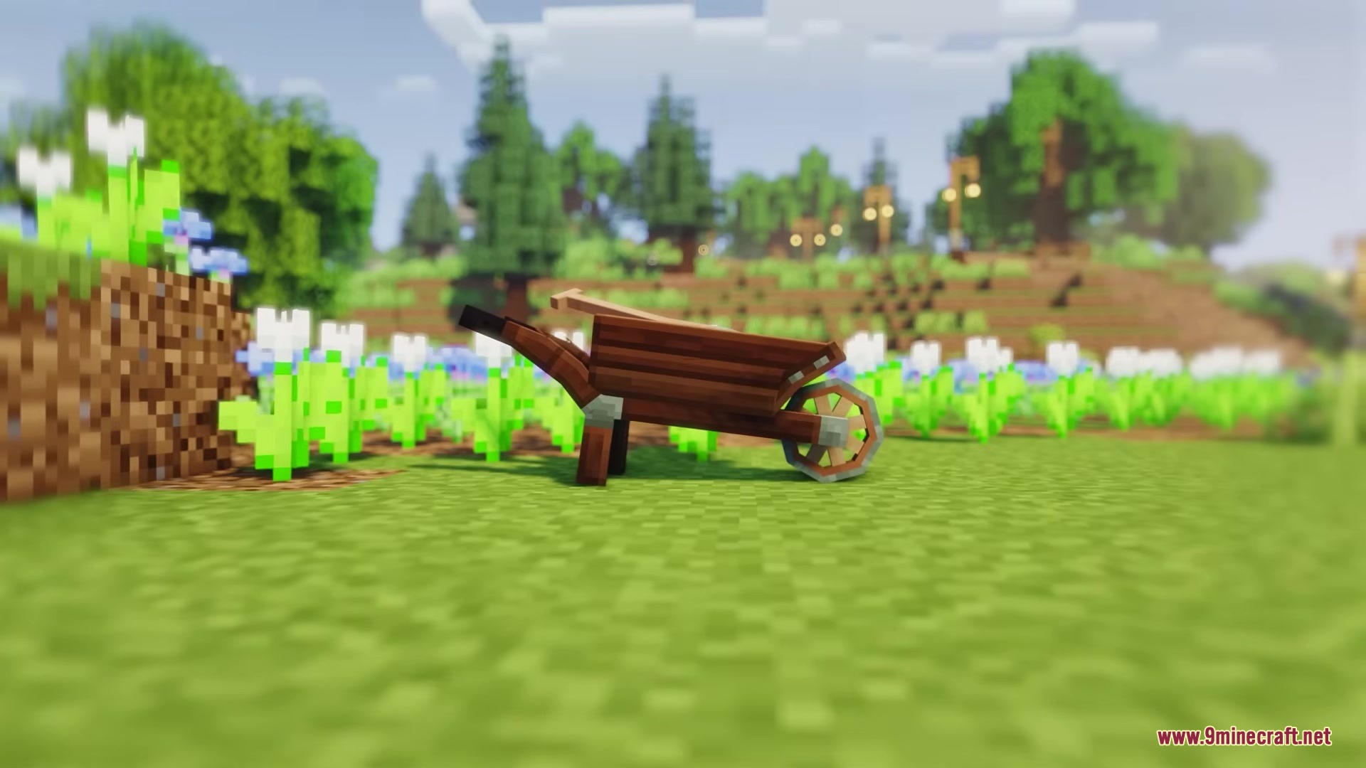 A wooden wheelbarrow sits on a grassy field with flowers and trees