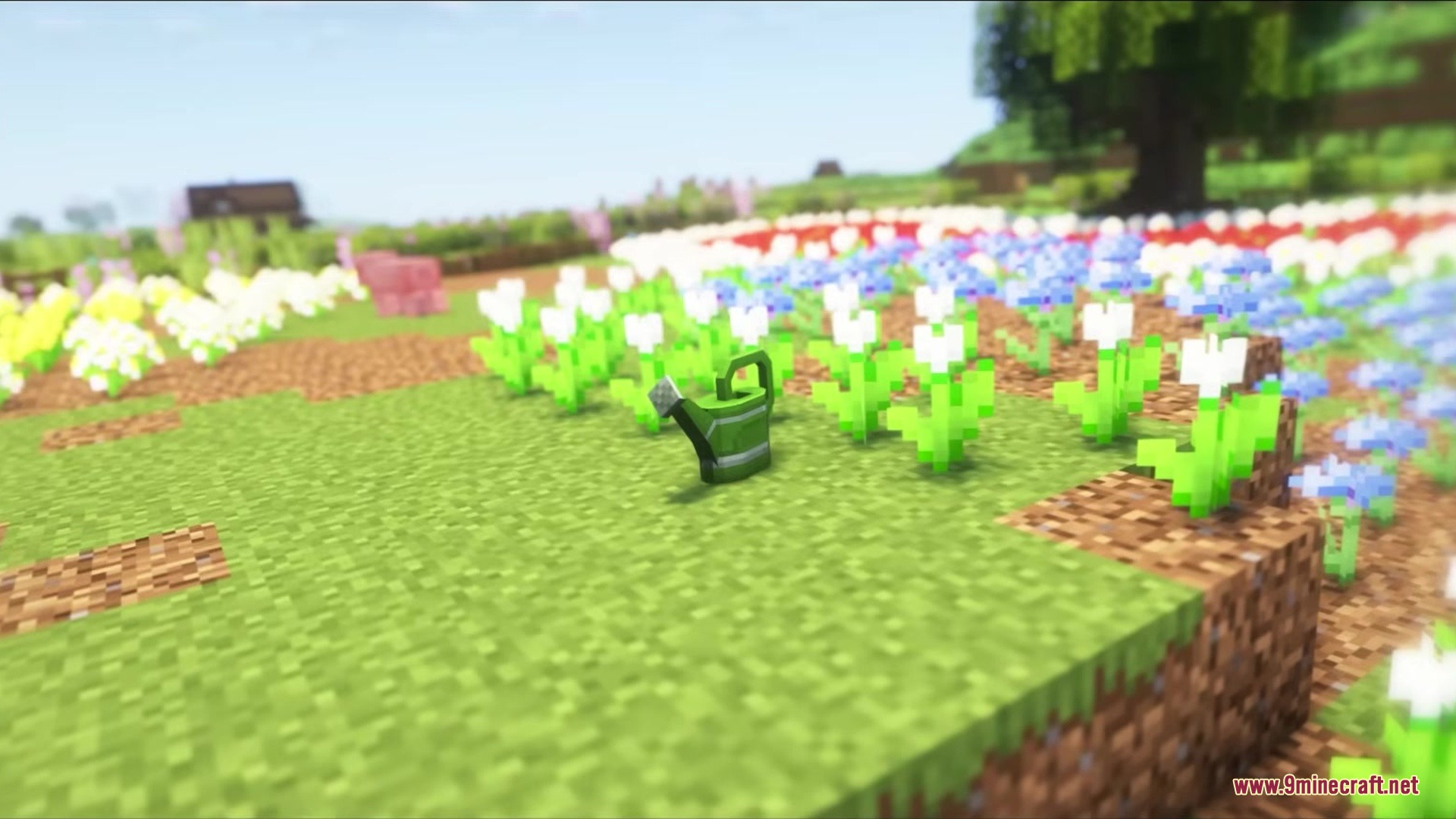 A green watering can placed on the grass in a colorful flower garden