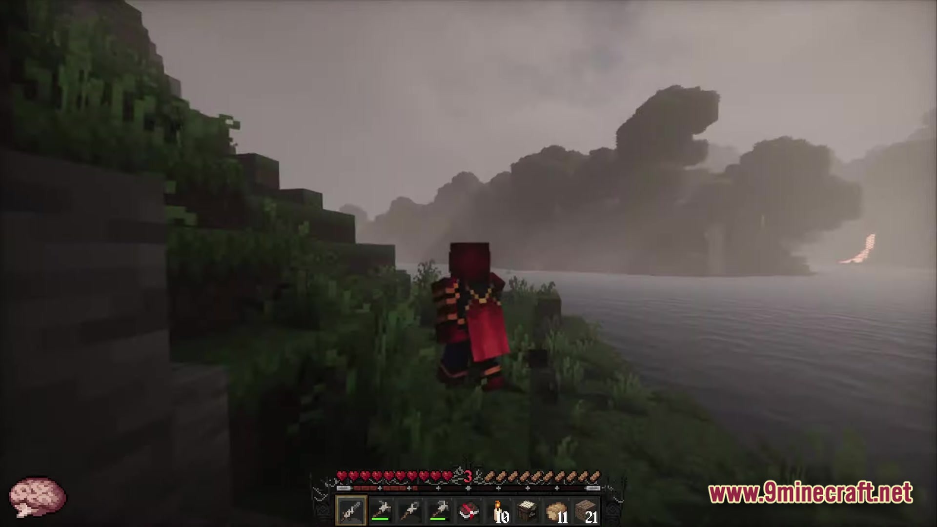 A player character in red armor stands on a grassy riverbank overlooking a foggy mountain landscape