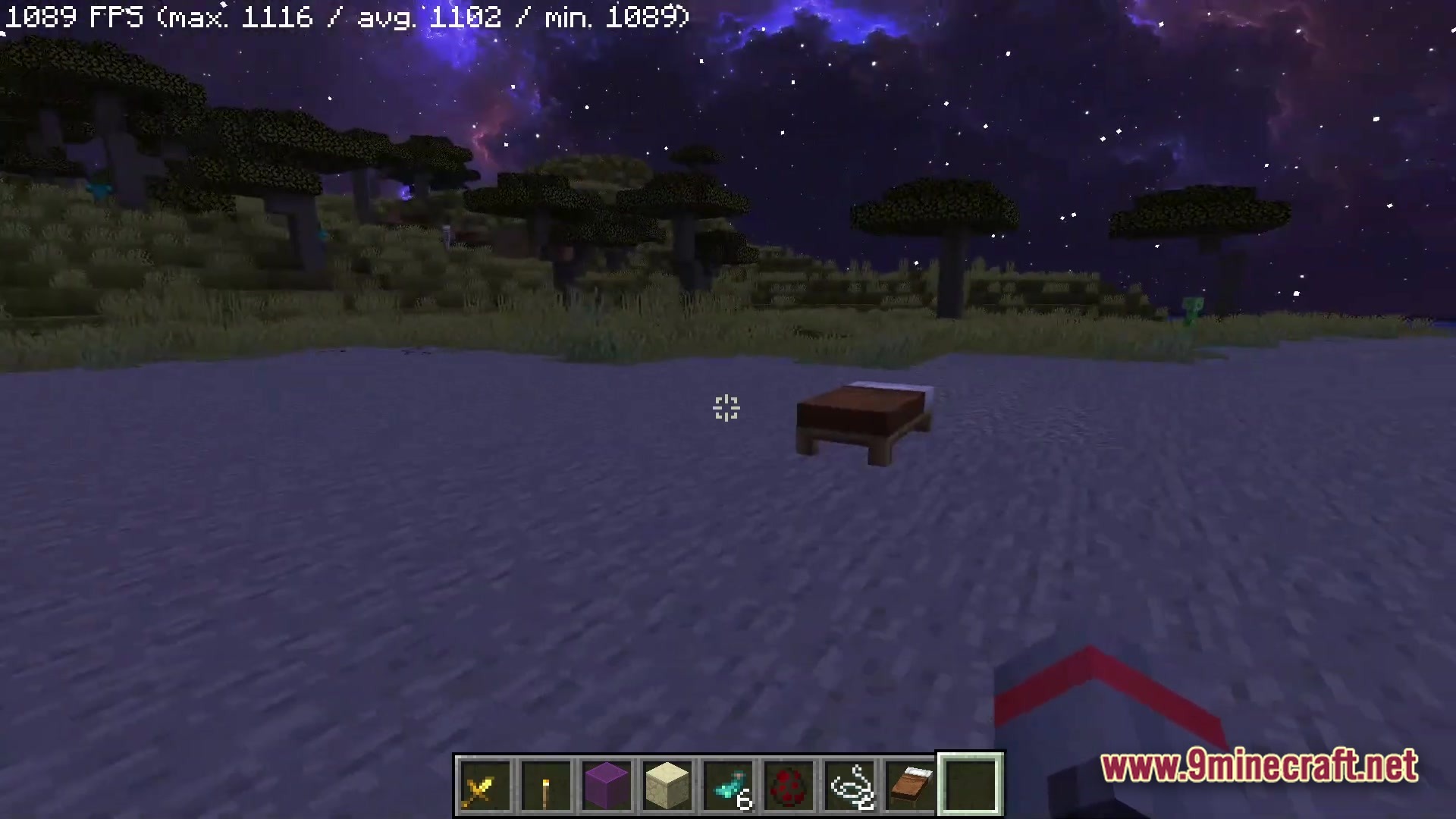 A brown bed sits on a beach under a purple nebula sky at night in Minecraft
