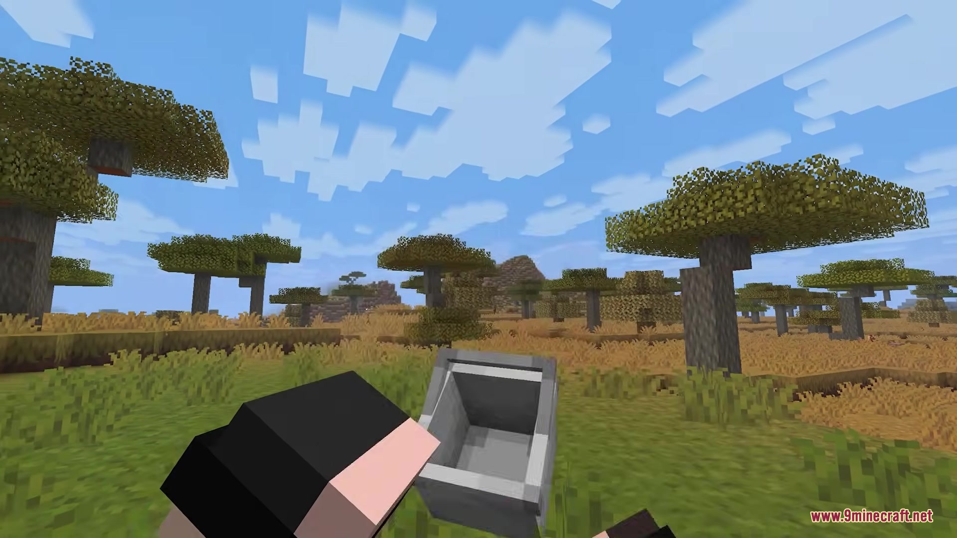 Player holding a 3D empty bucket while standing in a Minecraft savanna biome
