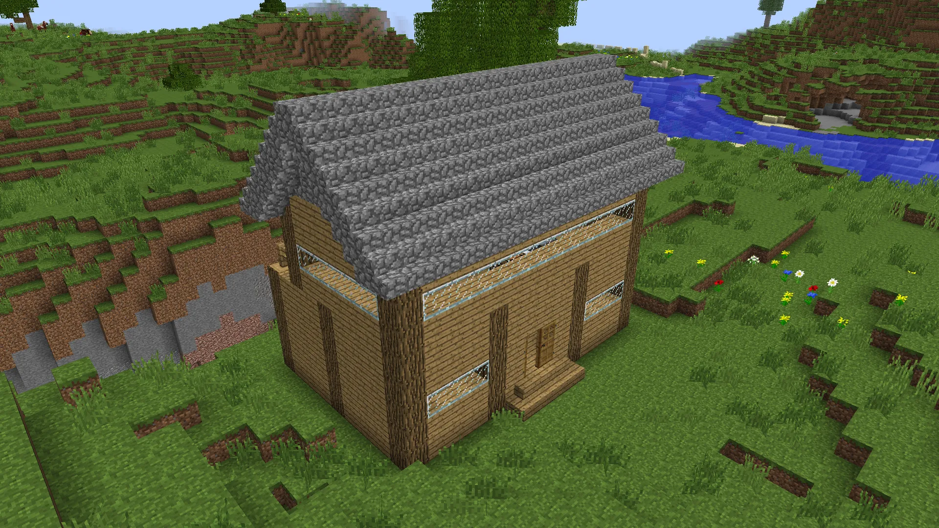 A simple wooden house with a cobblestone roof in a grassy field