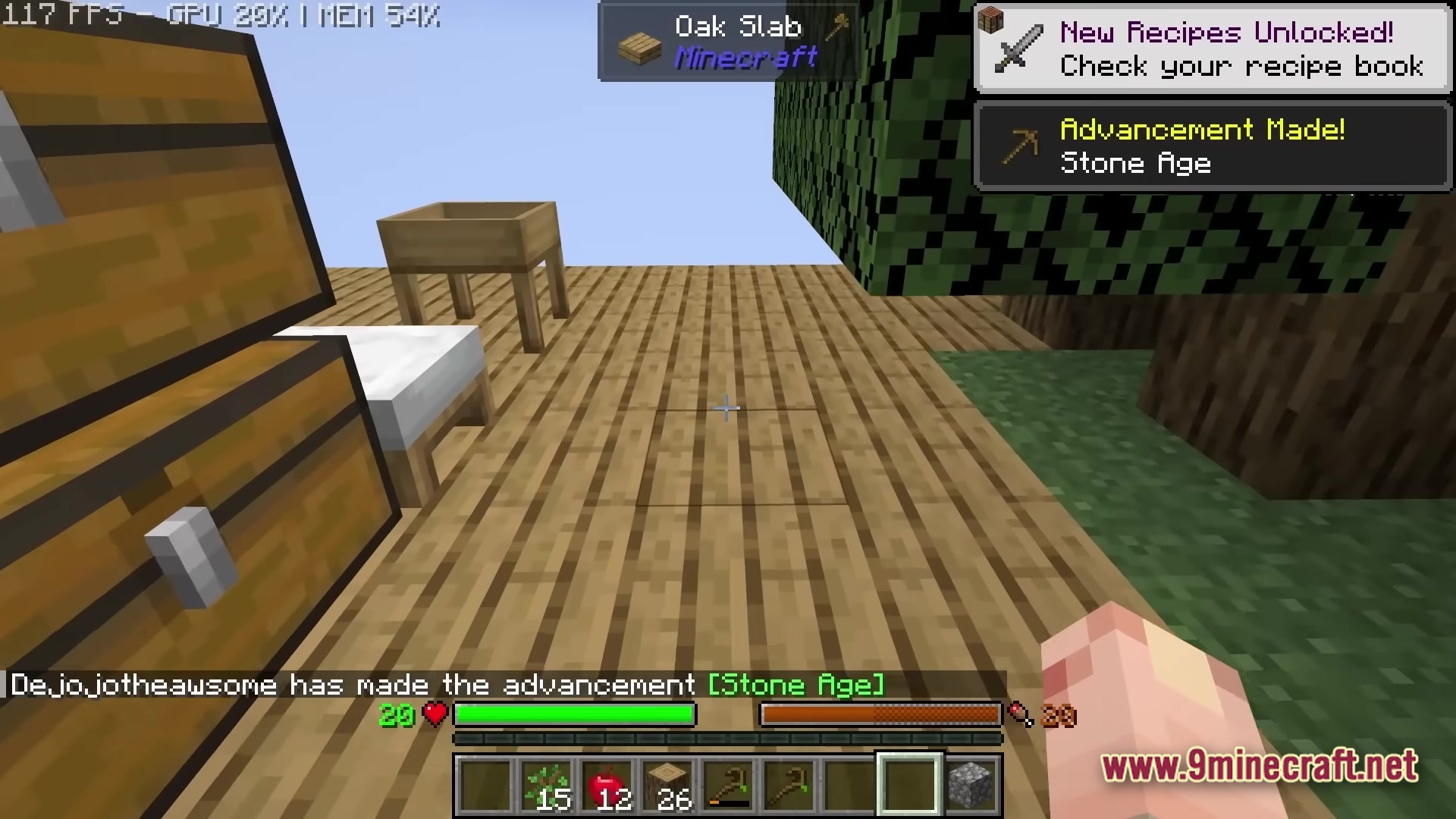 A player stands on a wooden platform near chests, a bed, and a tree in Skyblock