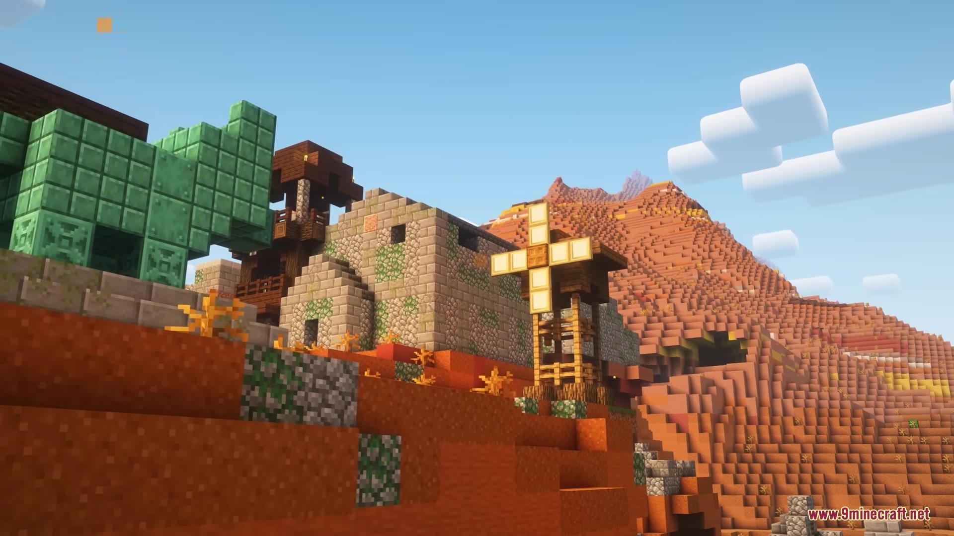 Stone houses and a windmill stand in a desert with red rocky mountains