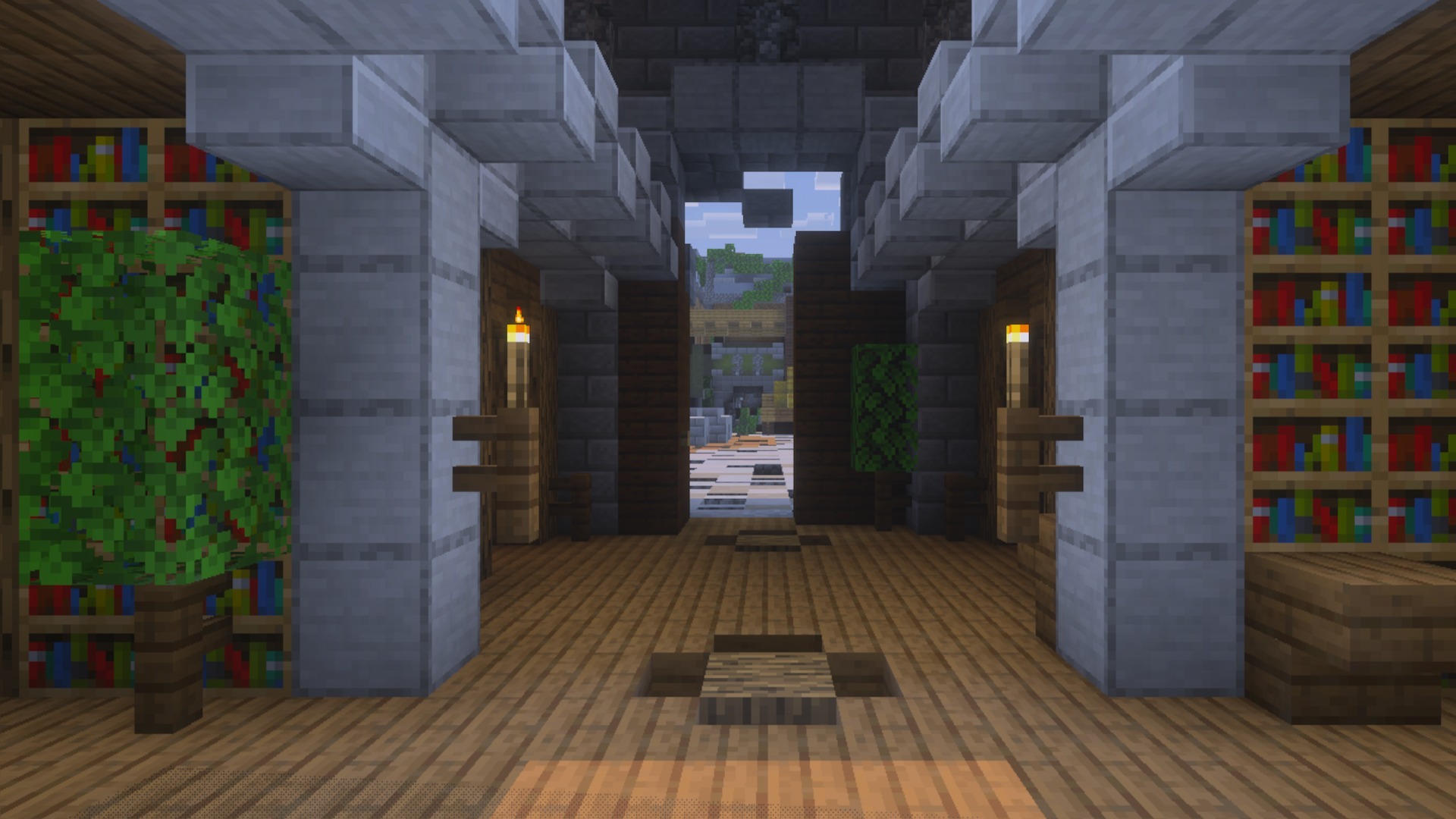 Interior of a stone hallway with wooden floors bookshelves and lit torches