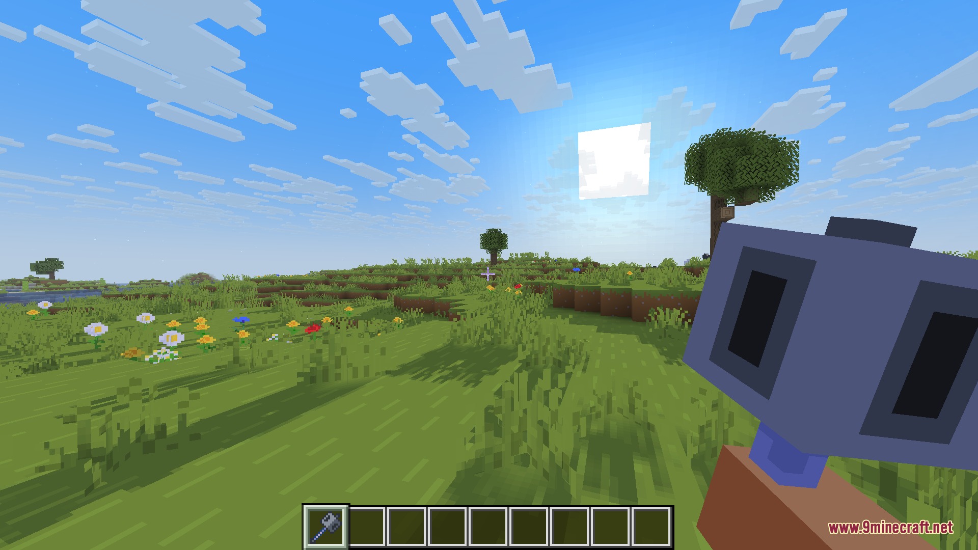 A player holds a blocky 3D mace tool while exploring a grassy field