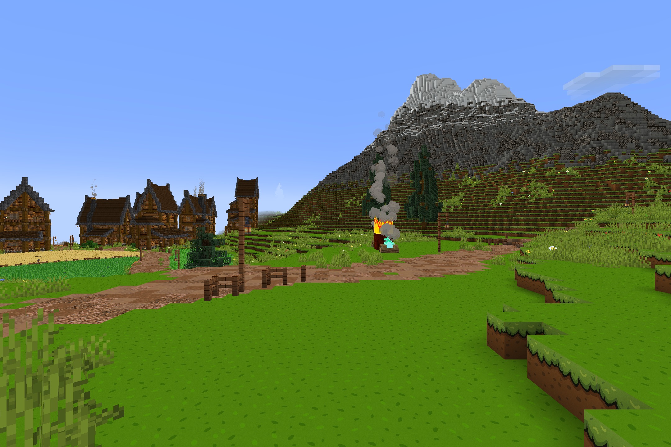 CartoonCraft Resource Pack Screenshot 2 Simple wooden houses and a smoking campfire near a large snowy mountain