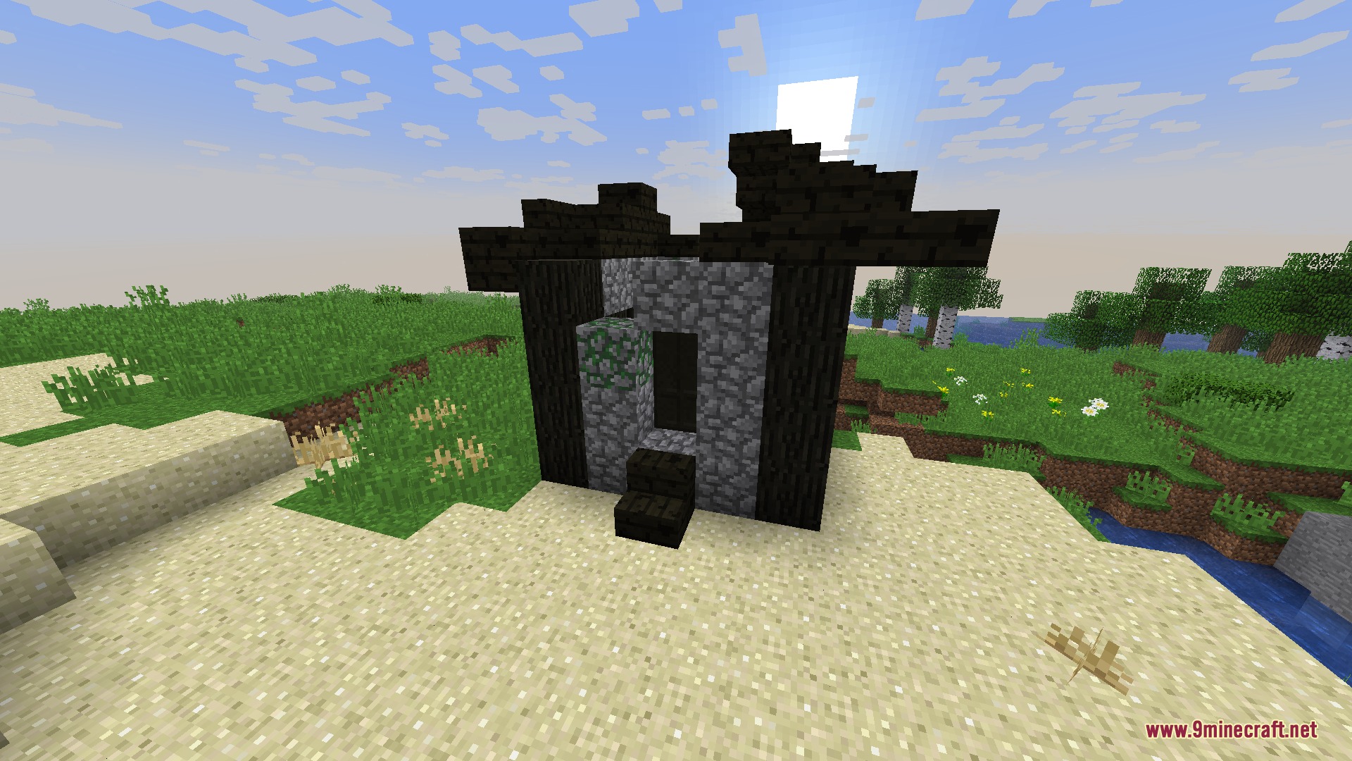 A small ruined building made of dark wood and cobblestone on the sand
