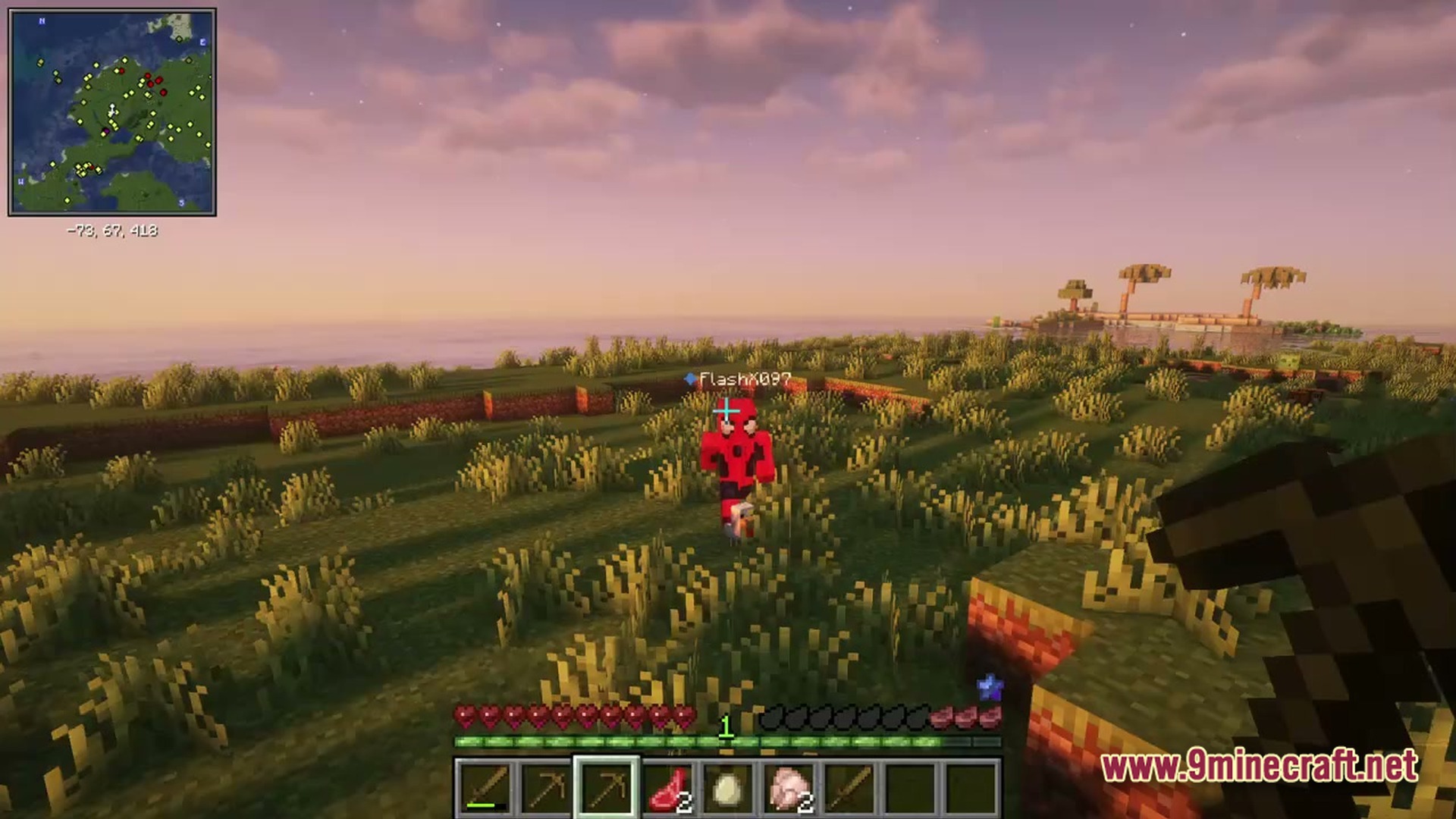A player in a red suit stands in a grassy field during sunset near the ocean