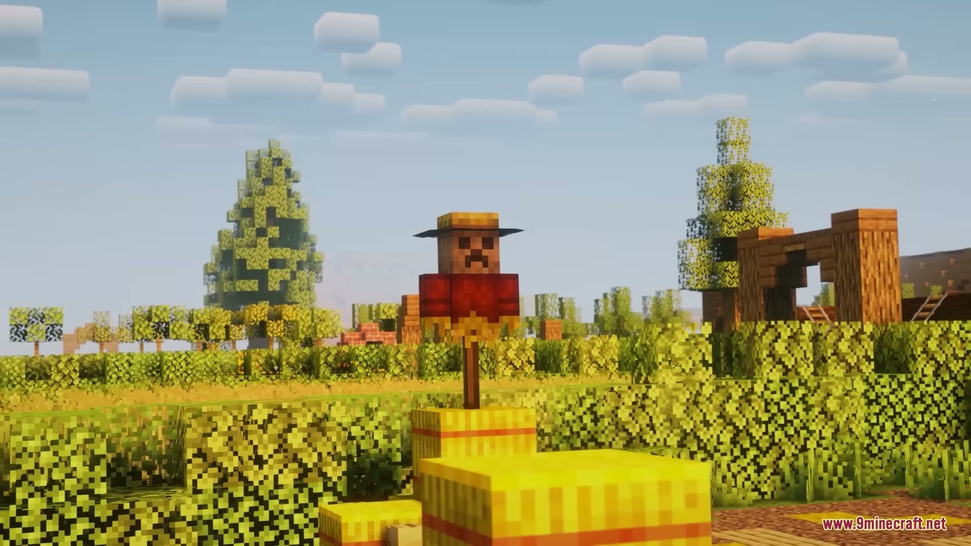 A scarecrow stands on hay bales to protect crops in a sunny field