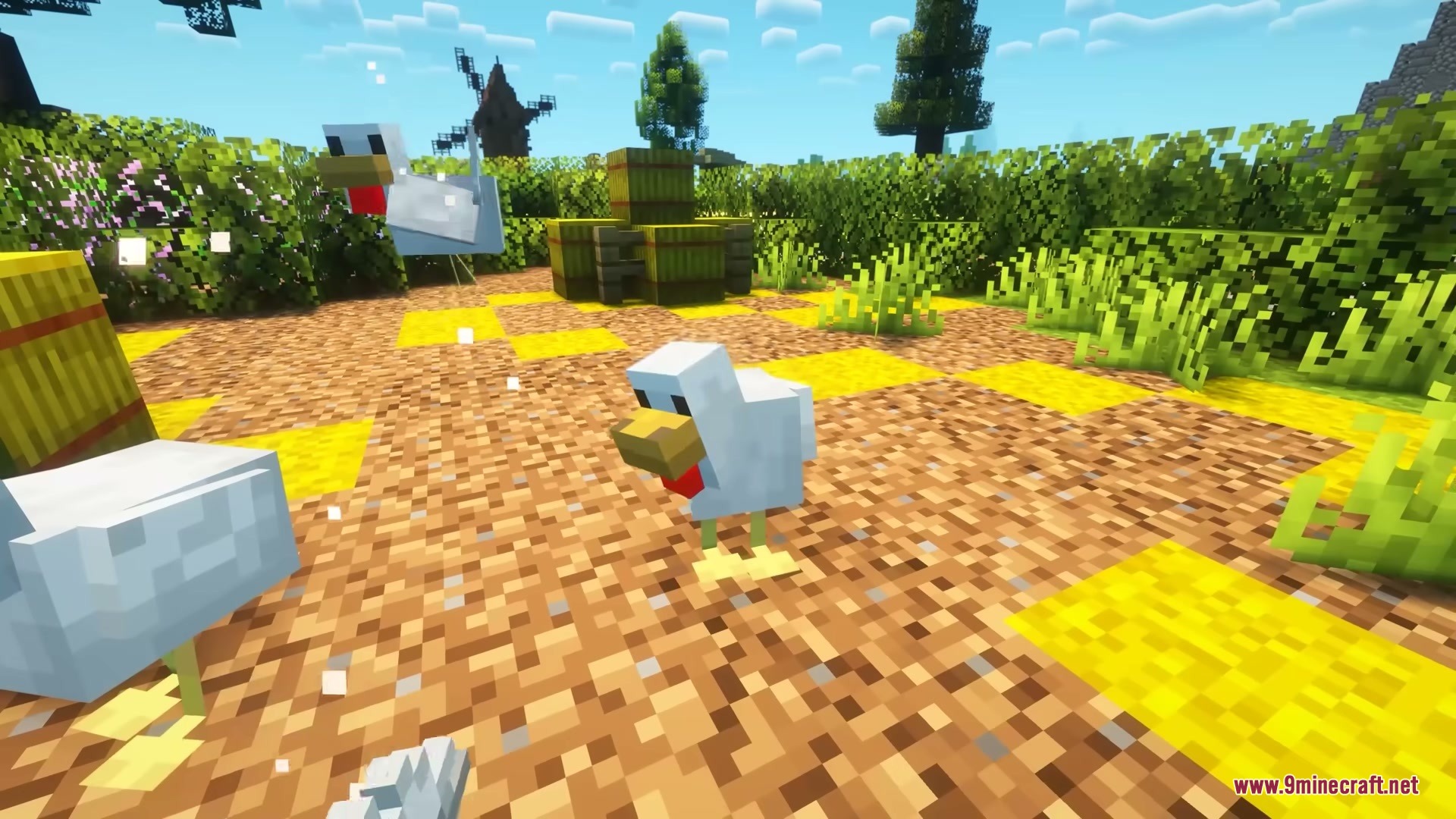 White chickens roaming a sunny farmyard with hay bales and green bushes