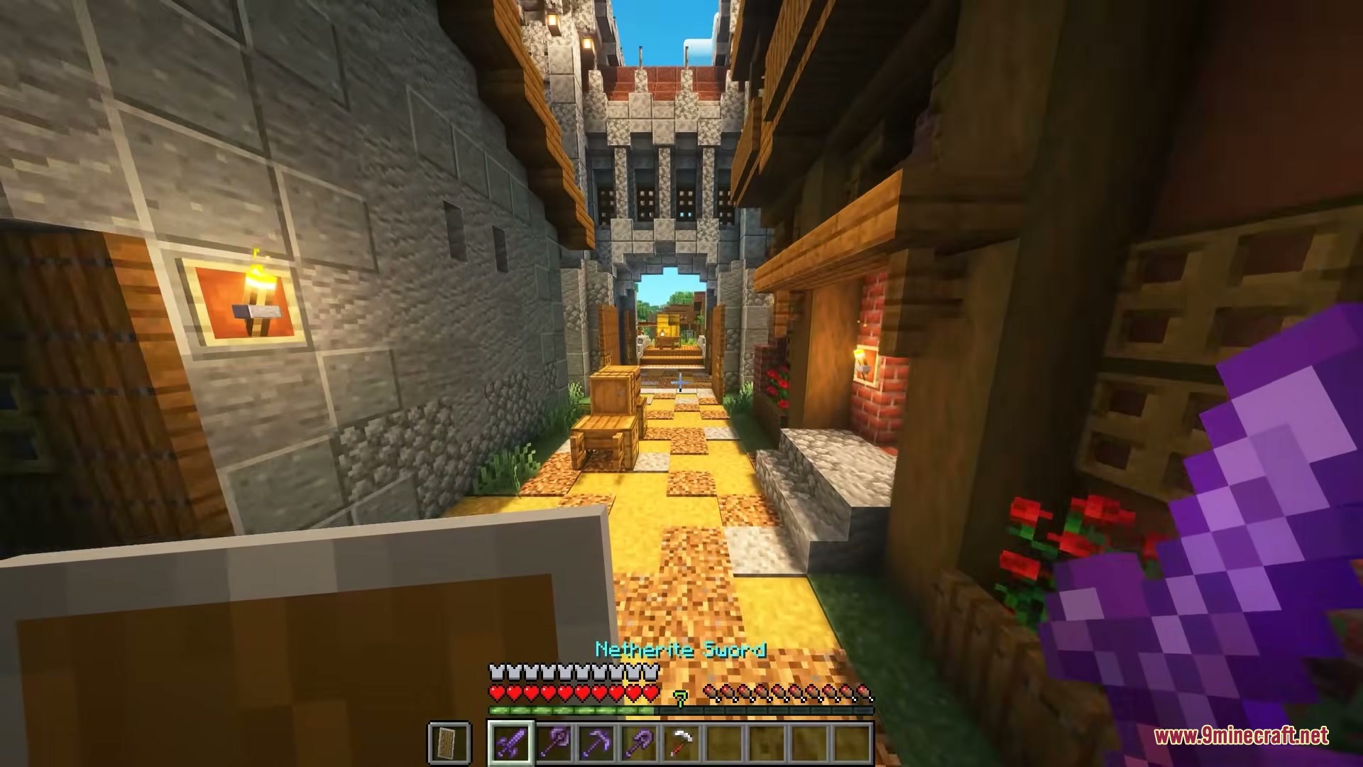 Player walks through a narrow stone street holding a netherite sword and shield
