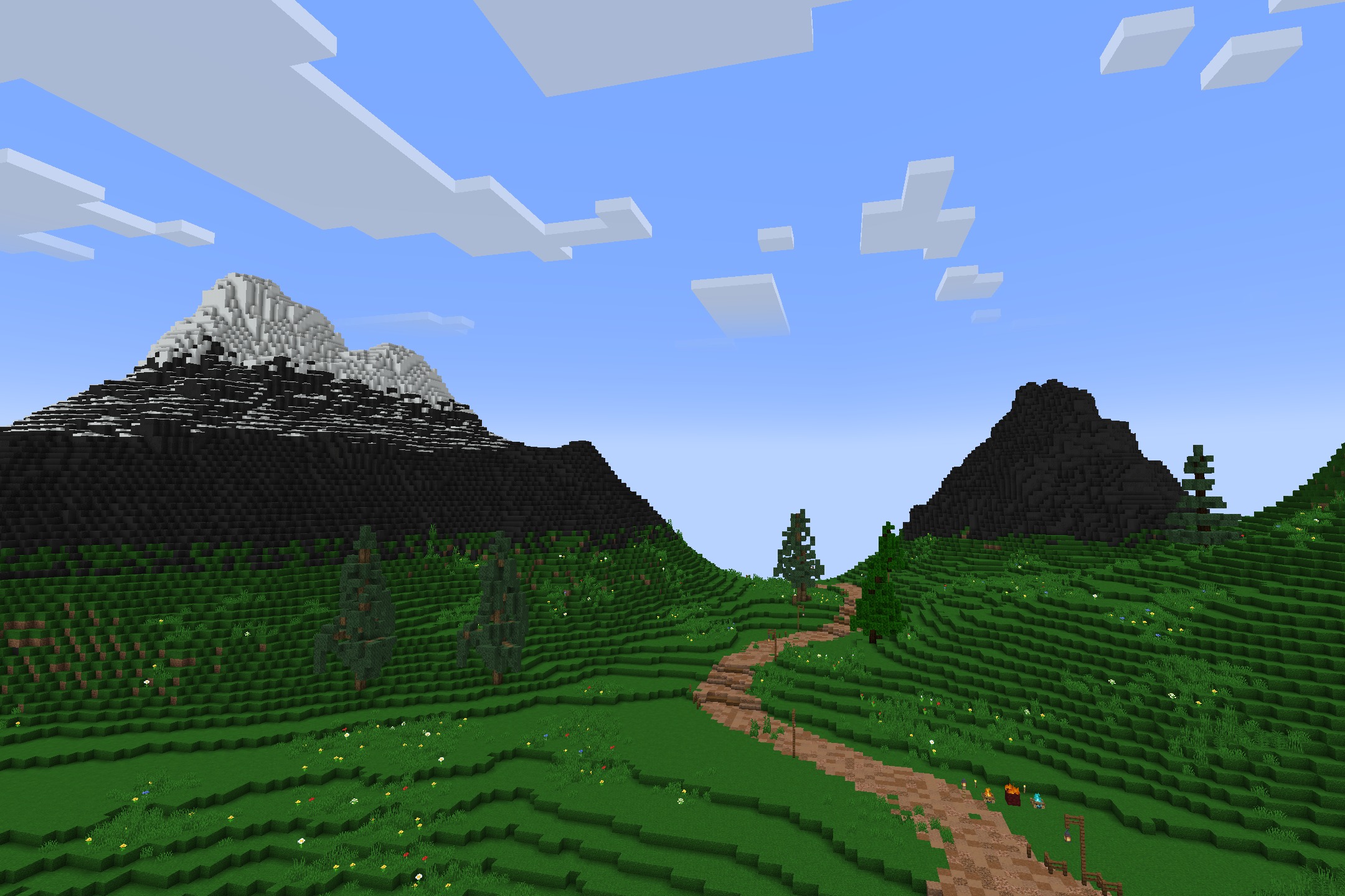 Green valley with a dirt path leading toward snowy mountain peaks