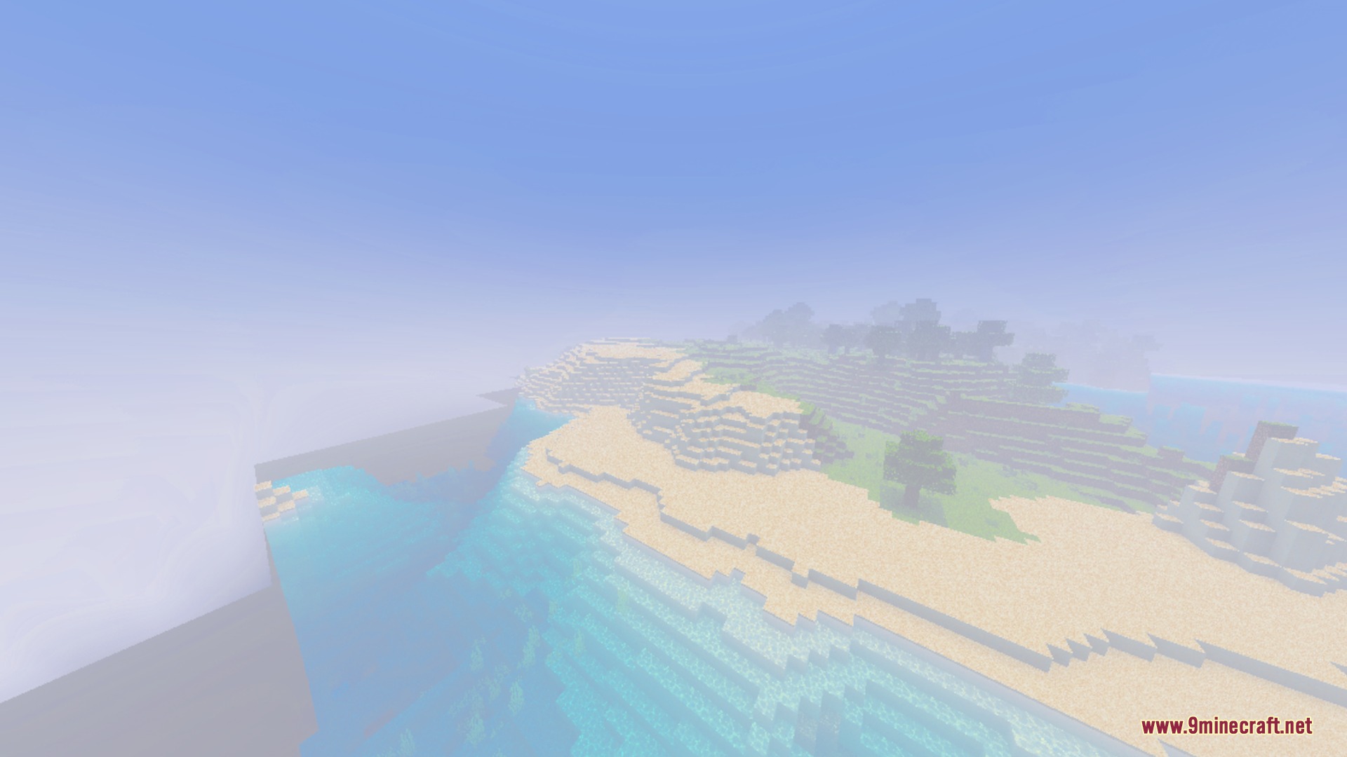 Soft white fog drifts over a sandy beach and clear blue water
