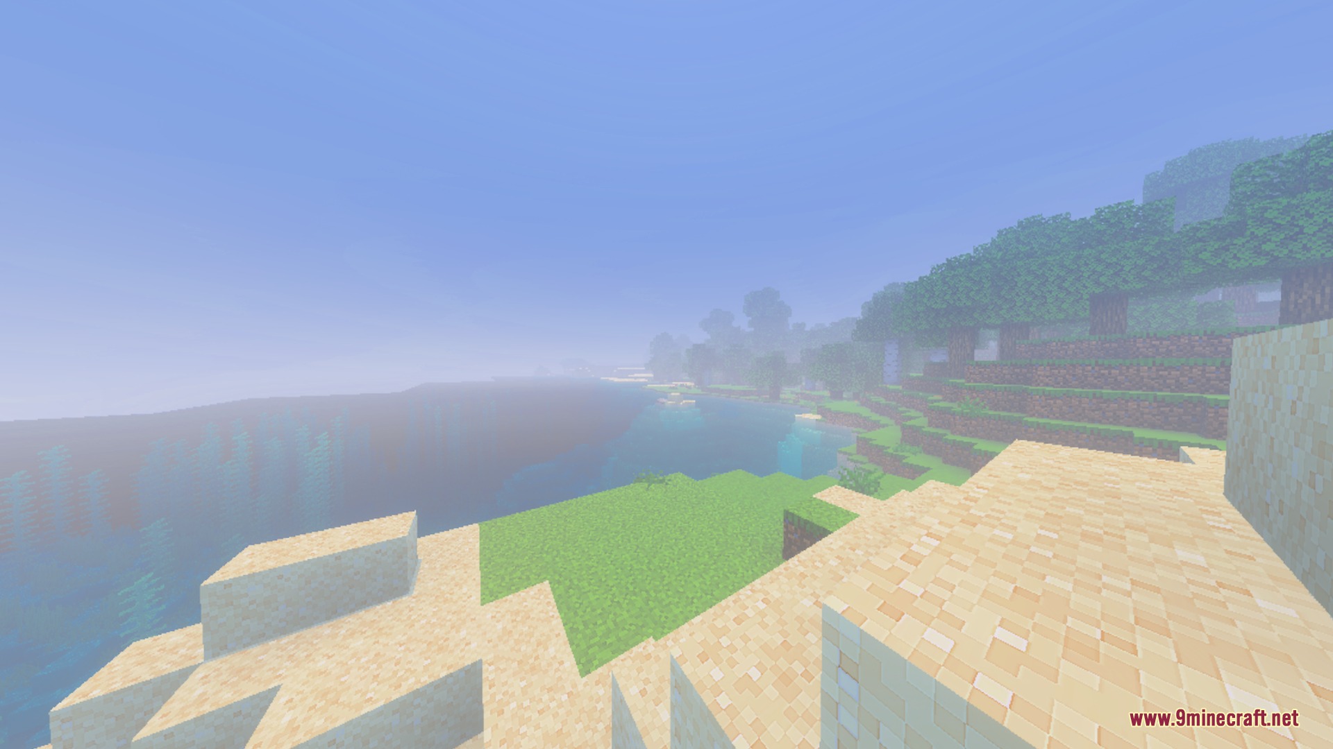A thick mist blankets the sandy beach and calm blue ocean water