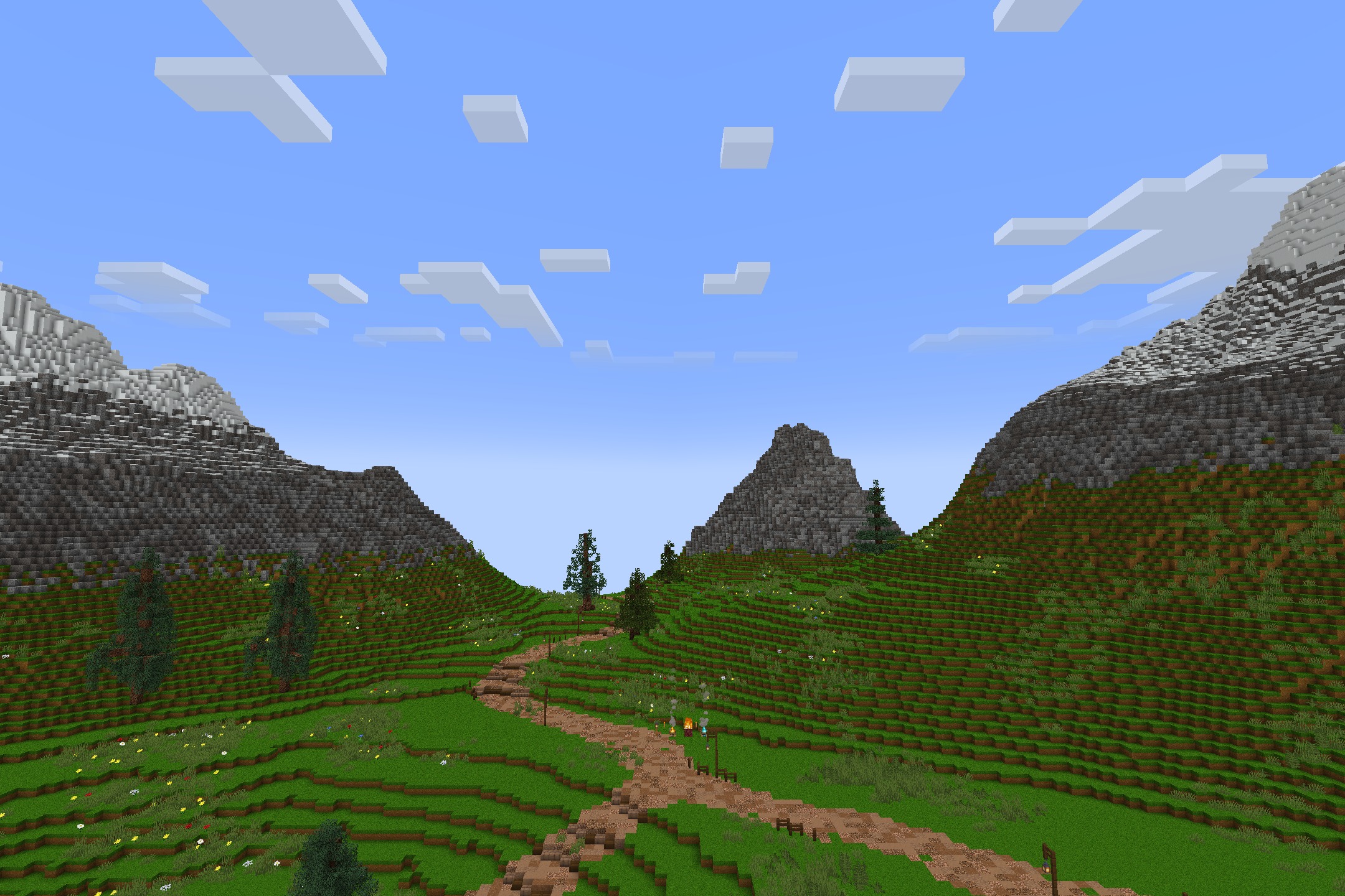 A winding dirt path through green hills leading towards tall mountains and trees