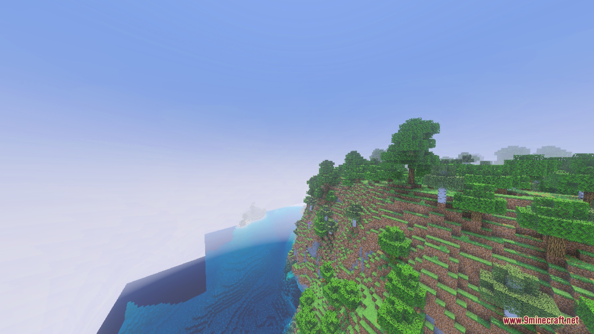 A steep grassy cliff with trees overlooking a foggy blue ocean horizon