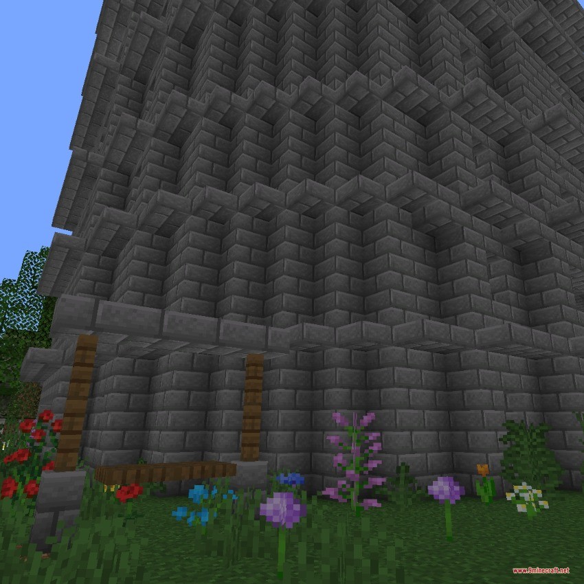 A tall stone brick tower structure with flowers growing at the base