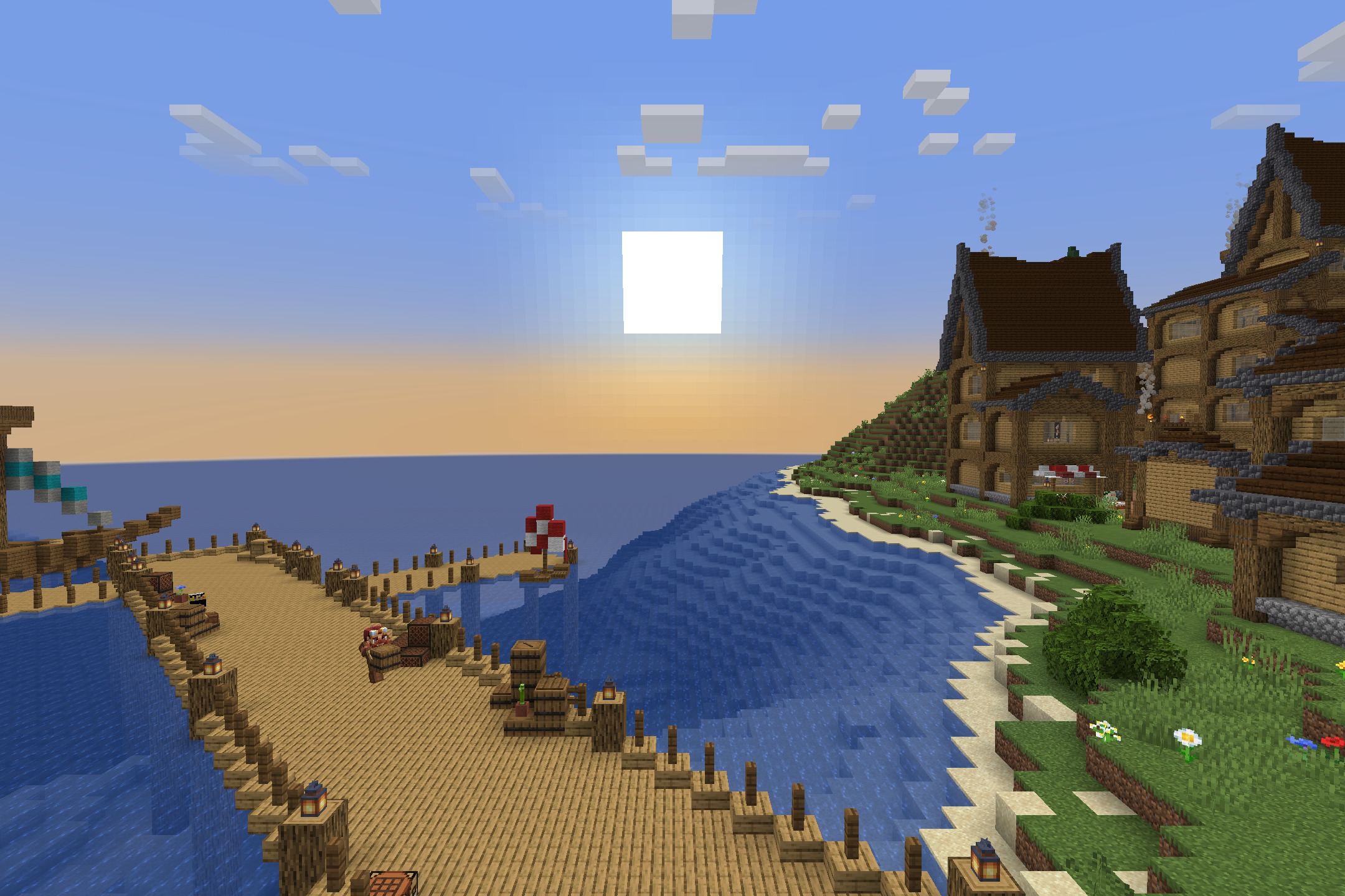 A wooden dock extends into the ocean next to a coastal village at sunset
