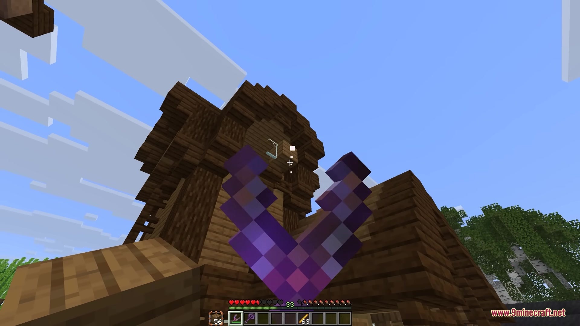 Simply Slingshot Mod Screenshot 7 Player aiming an enchanted slingshot at a tall wooden building in Minecraft