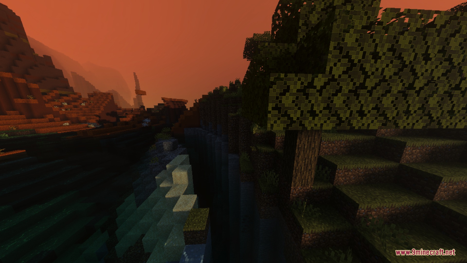 A deep ravine separates a dark forest from rocky hills at sunset