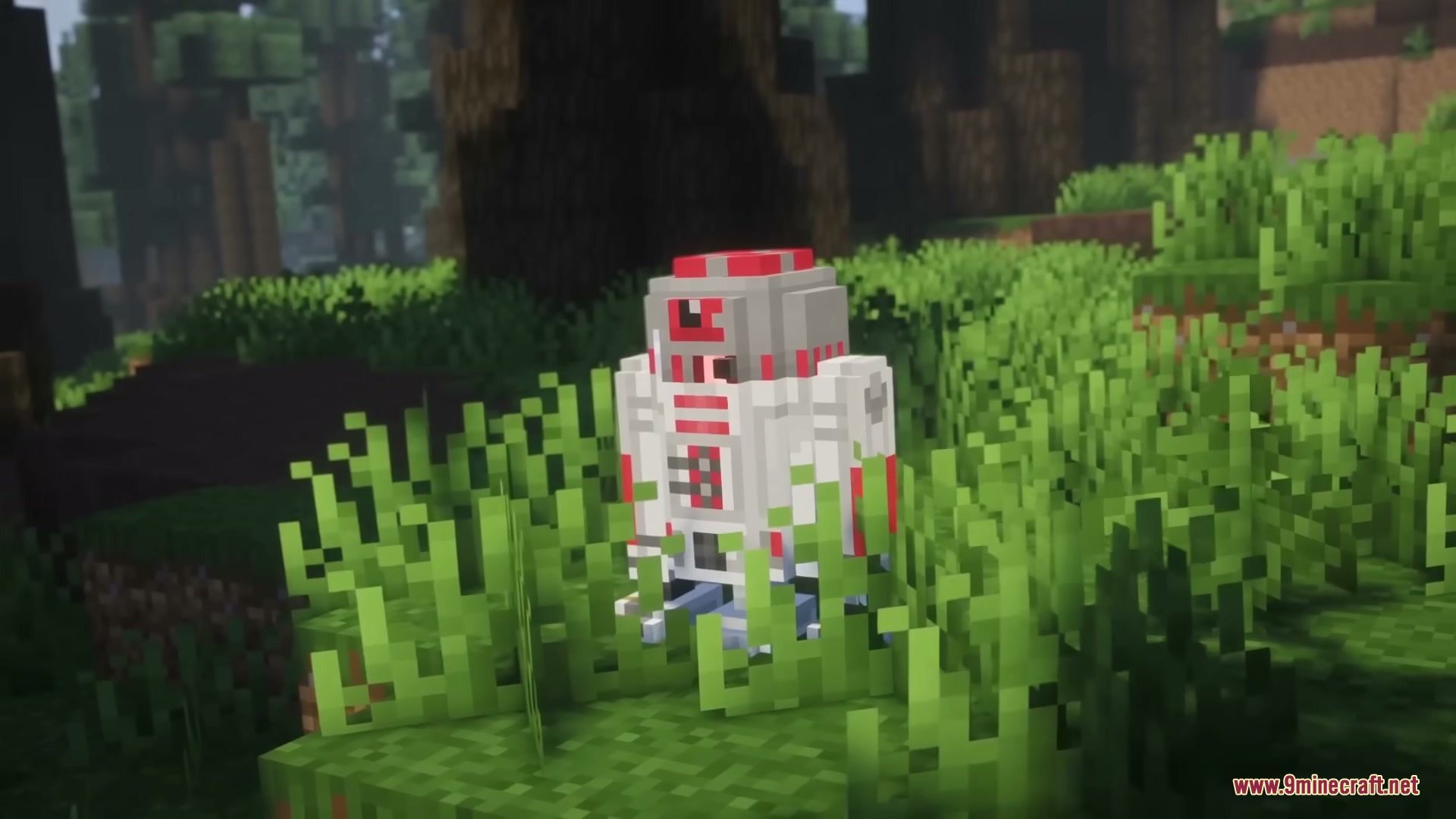 A small red and white astromech droid stands in the tall green grass