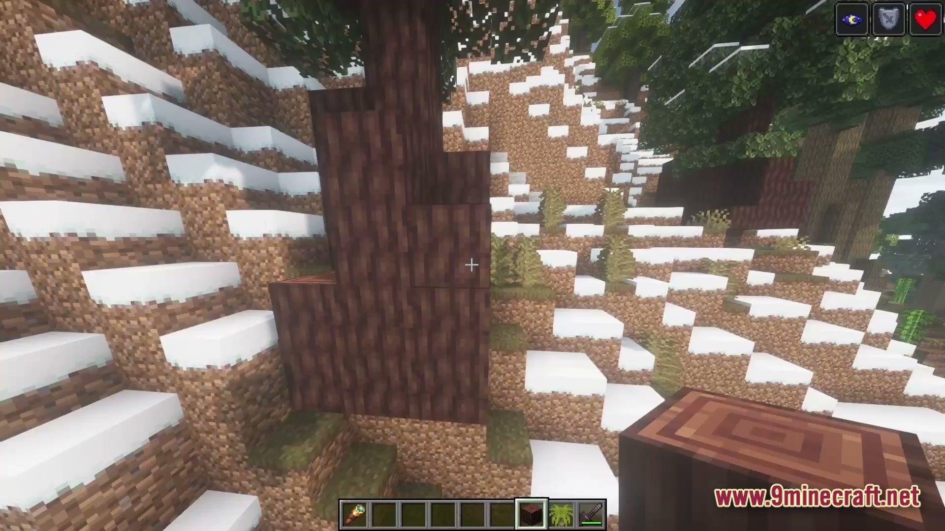 A player stands on a snowy hillside holding a dark wood log in a coniferous forest