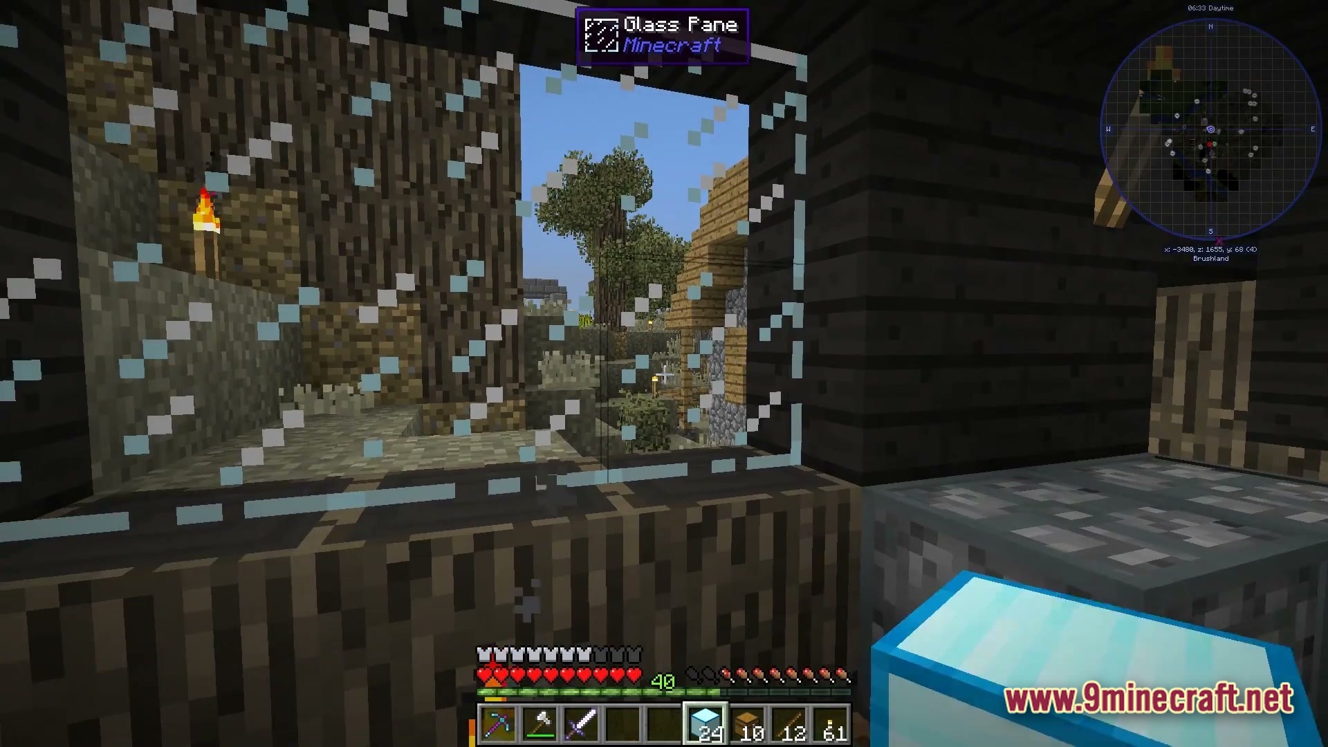 The Fool Modpack Screenshot 6 A first-person view through a glass pane window overlooking a brushland biome with wooden structures